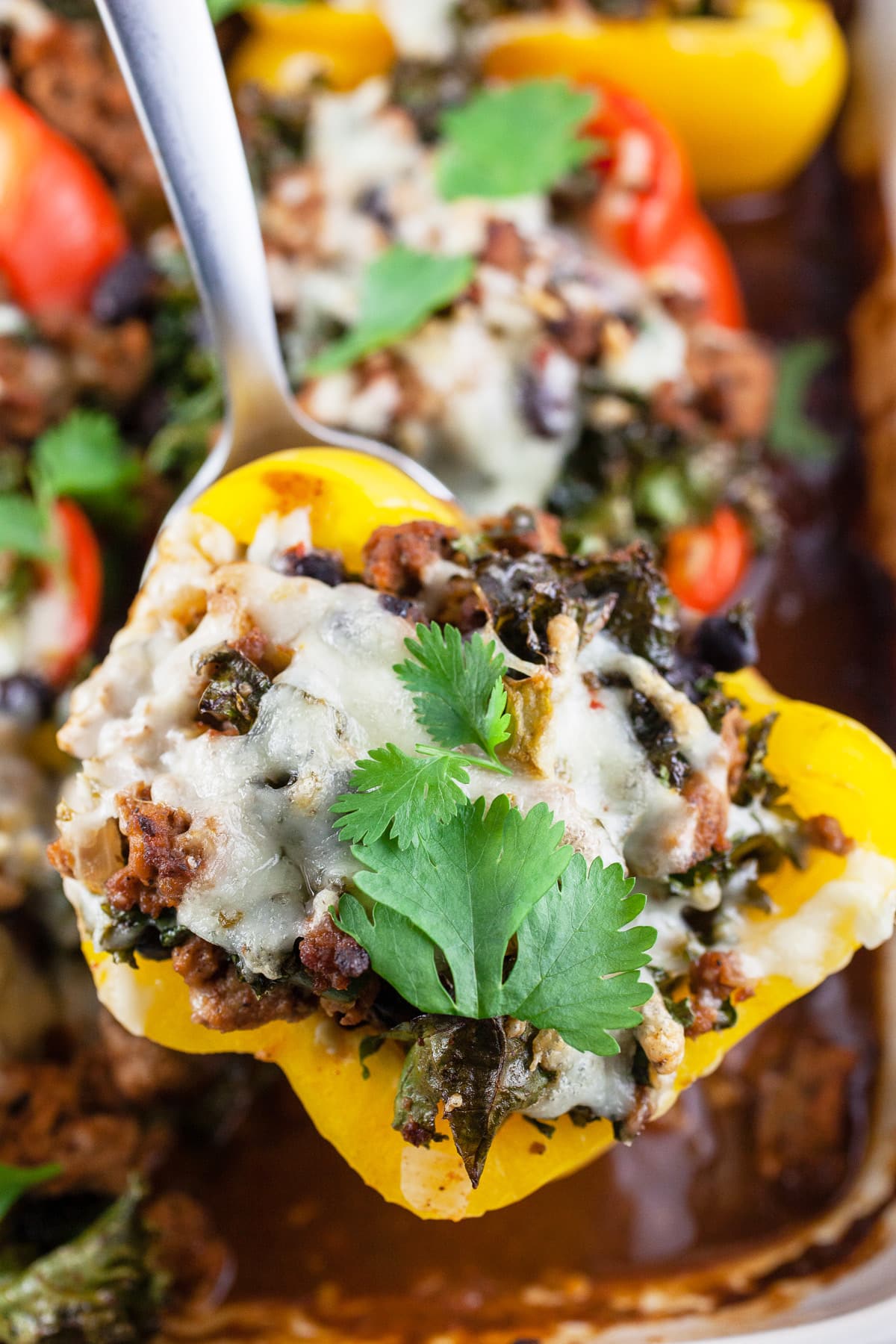 Large spoon lifting stuffed yellow bell pepper from baking dish.