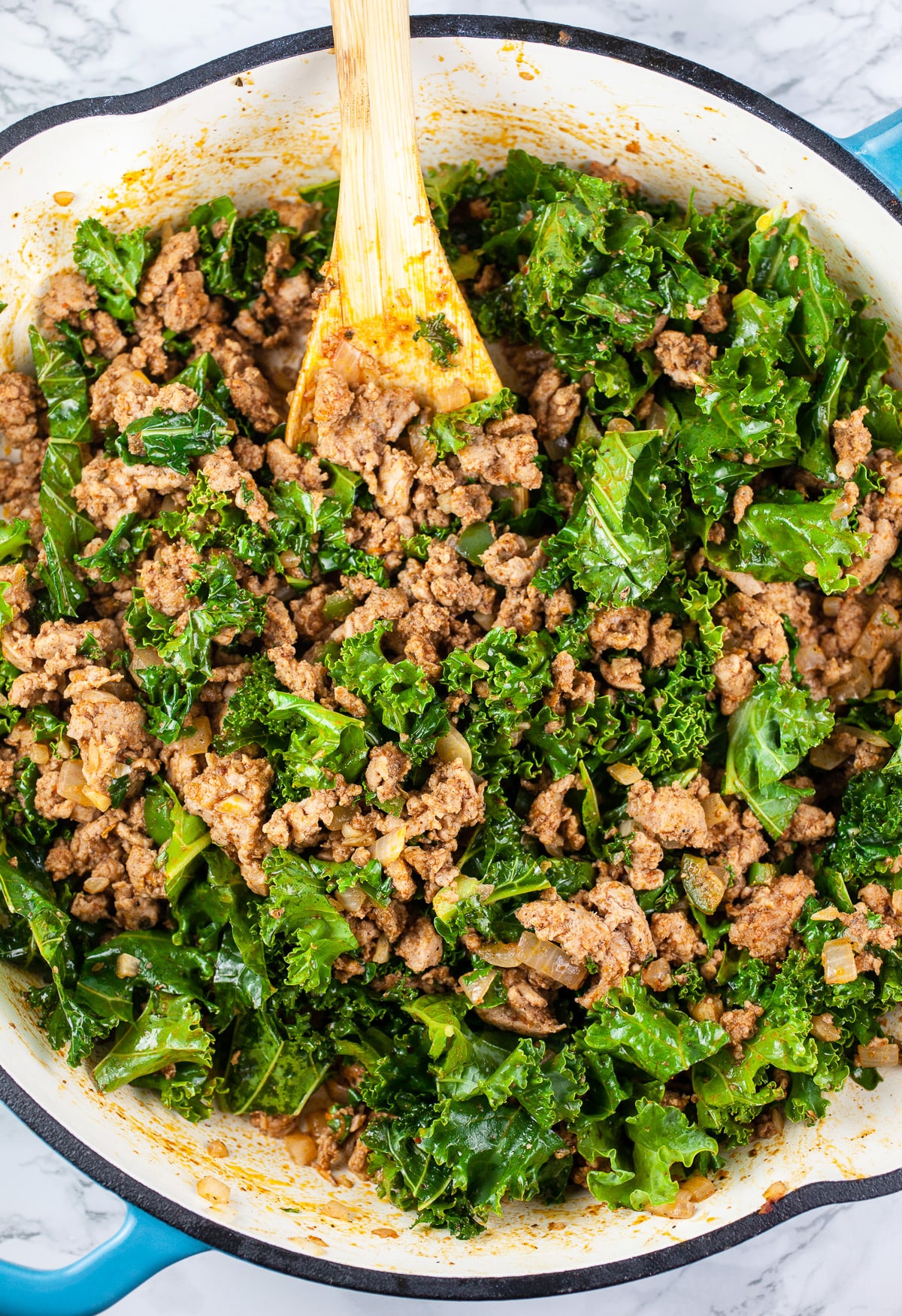 Ground turkey and kale sautéed in skillet.