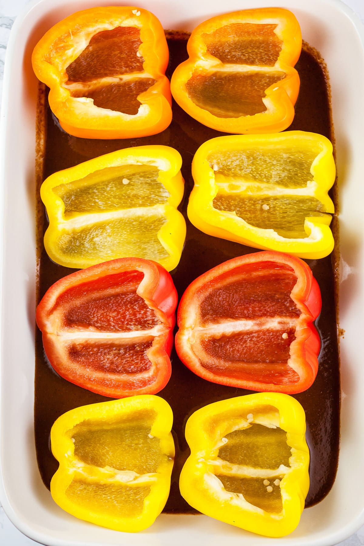Bell pepper halves and red enchilada sauce in baking dish.