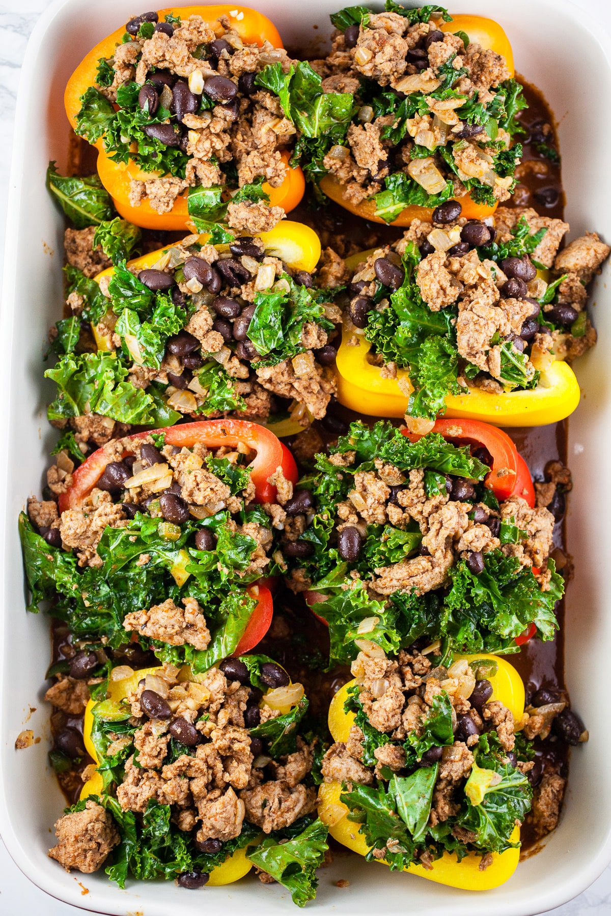 Uncooked stuffed bell peppers and enchilada sauce in baking dish.