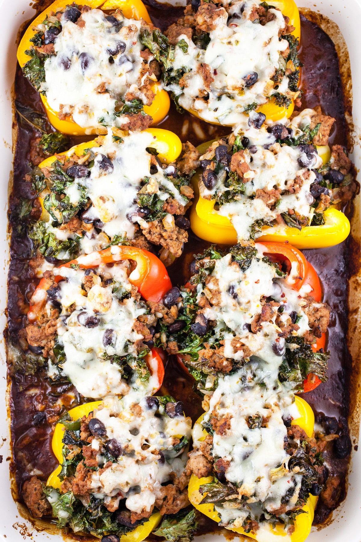 Stuffed peppers with melted cheese in baking dish with red enchilada sauce.