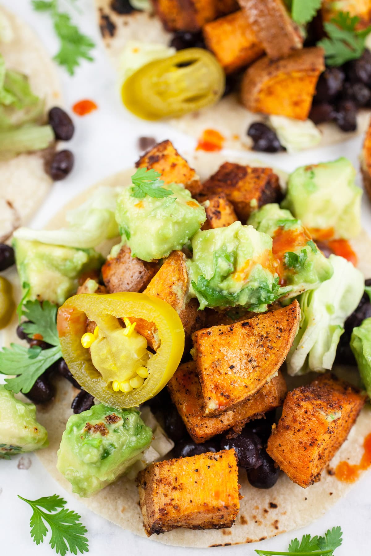 These Sweet Potato Tacos with Avocado Salsa make for a great weeknight dinner! This vegan sweet potato taco recipe is the perfect healthy clean eating dish. Sweet potatoes are topped with spices and then roasted until crispy in the oven. These vegetarian tacos are finished with black beans served with avocado salsa. Healthy eating doesn't get any easier than this! #sweetpotato #tacos #avocado #vegetarian #vegan Roasted sweet potato tacos with black beans, avocado salsa, and pickled jalapenos.