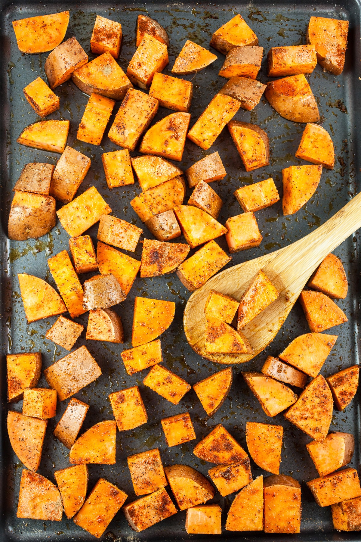 Uncooked diced sweet potatoes tossed in olive oil and spices on baking sheet.