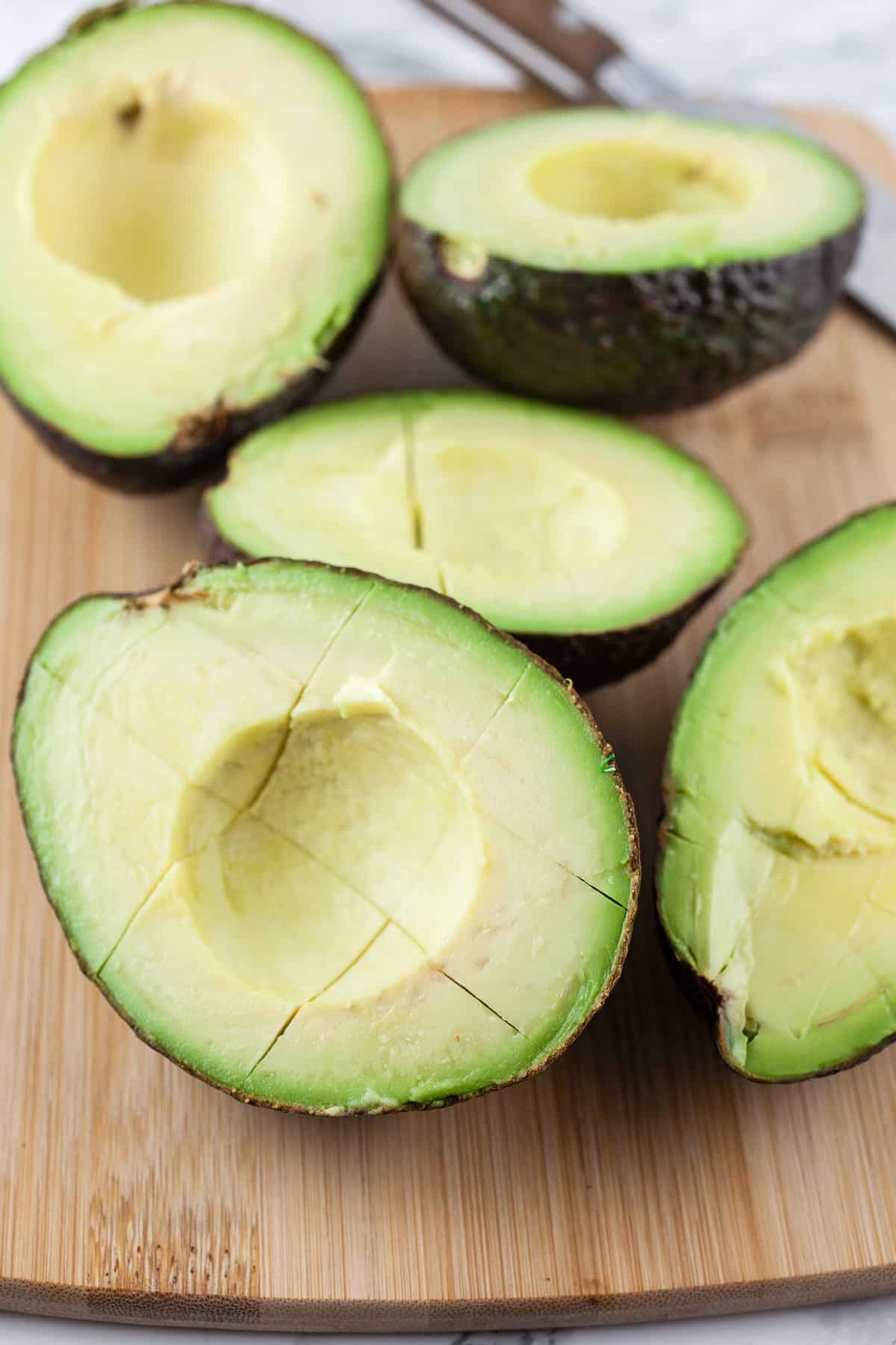 Avocadoes cut into halves and scored with knife on wooden cutting board.