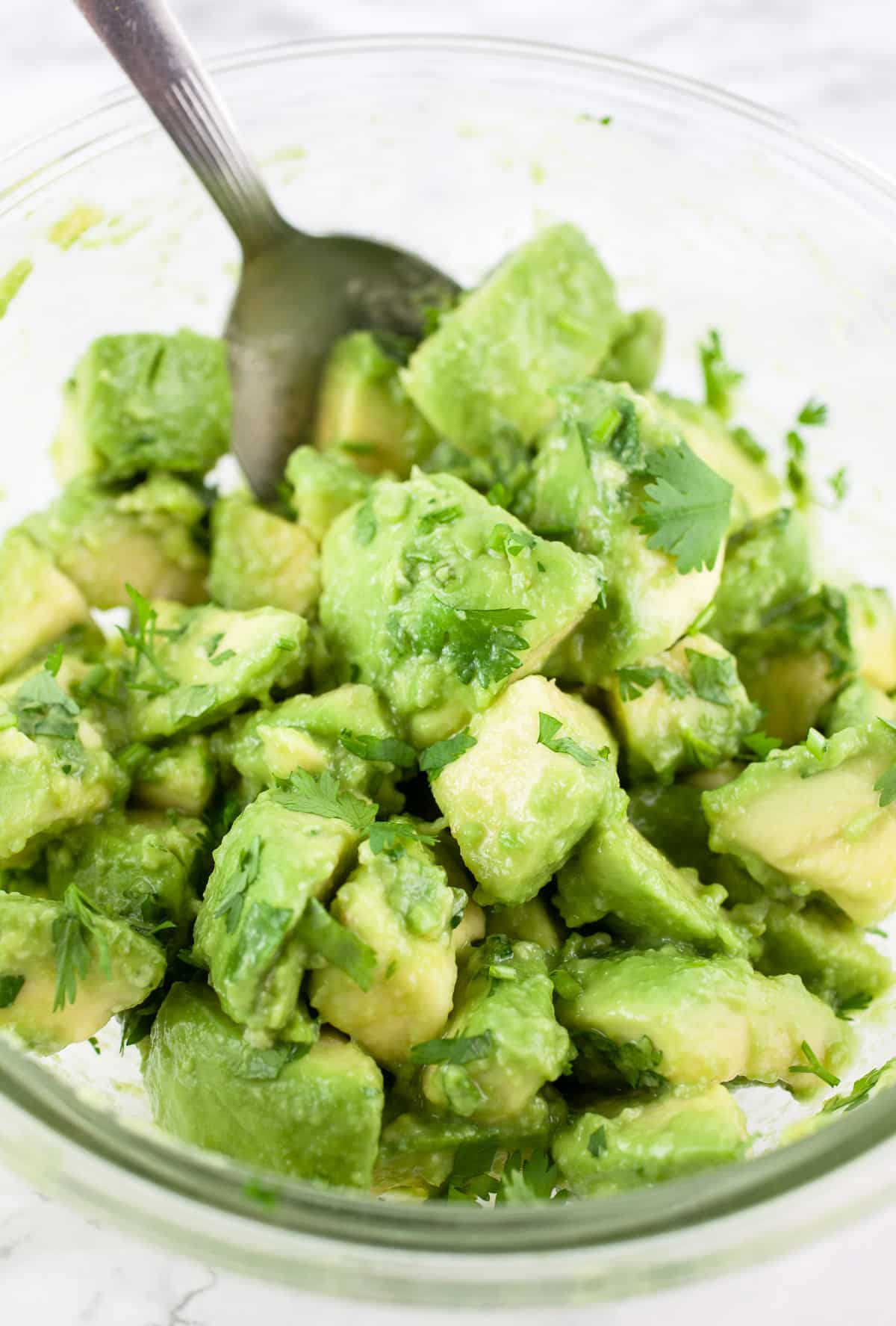 Avocado salsa in small glass bowl with spoon.