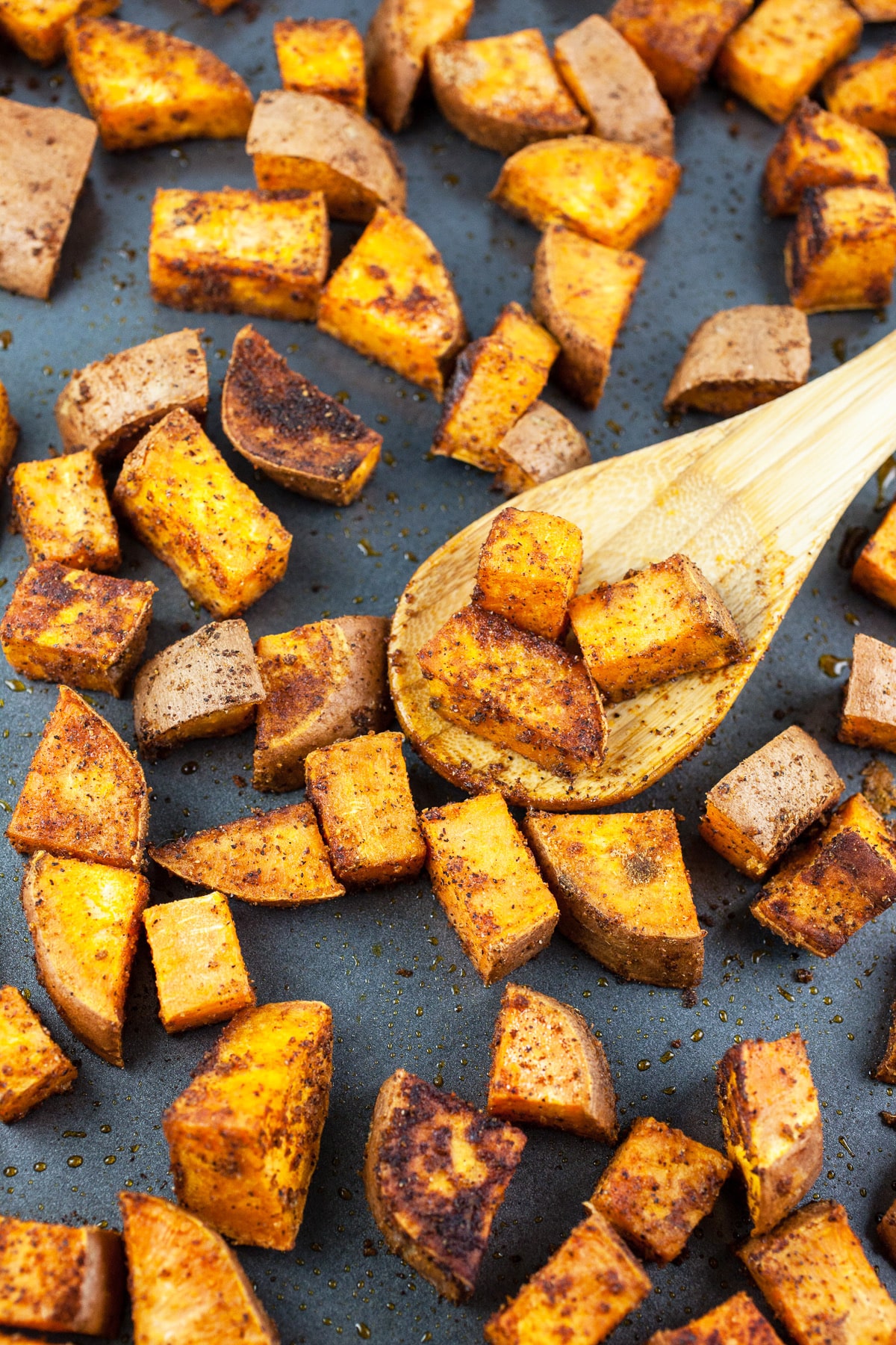 Roasted sweet potatoes on baking sheet with wooden spoon.