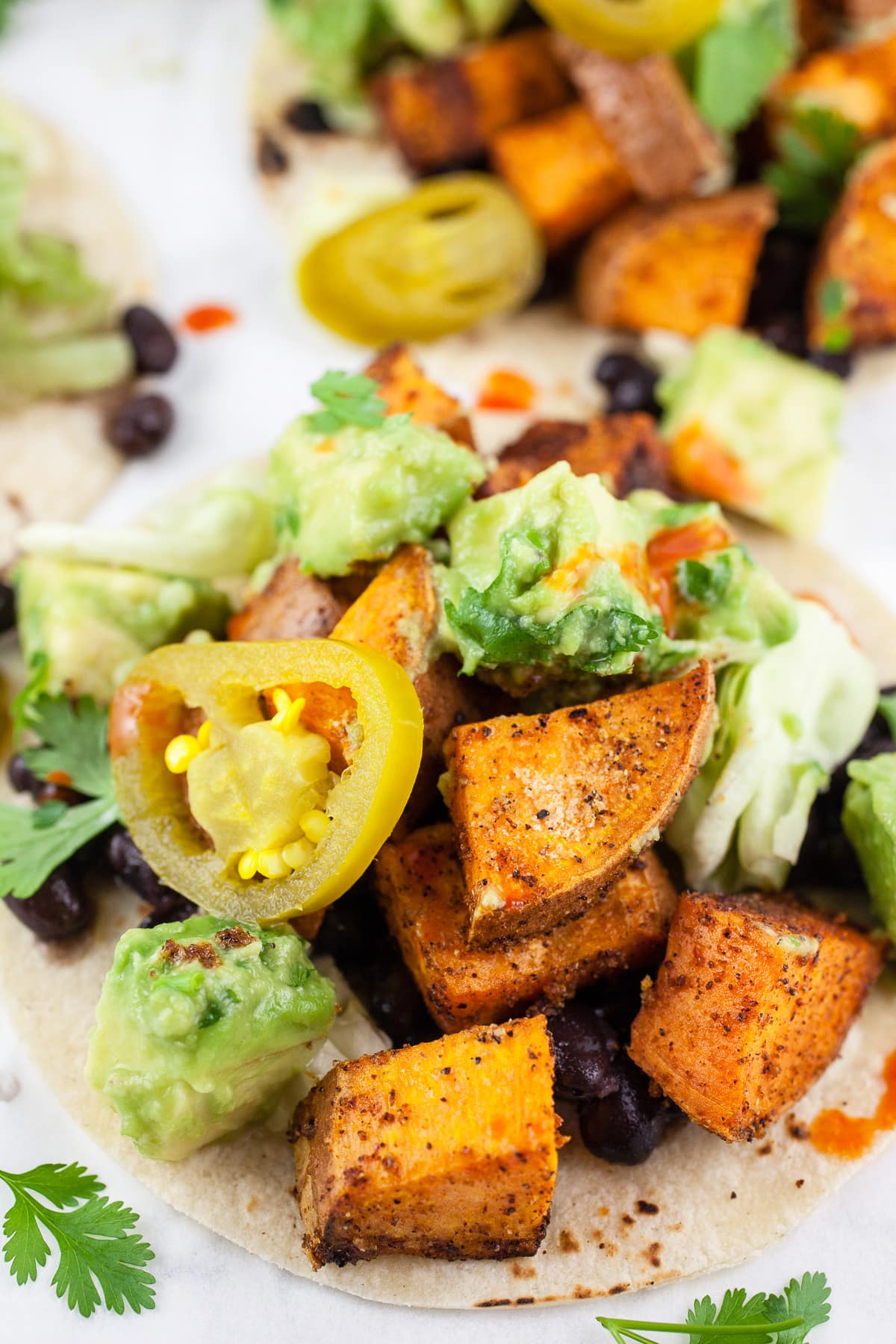 Roasted sweet potato tacos with black beans and avocado salsa on corn tortillas.