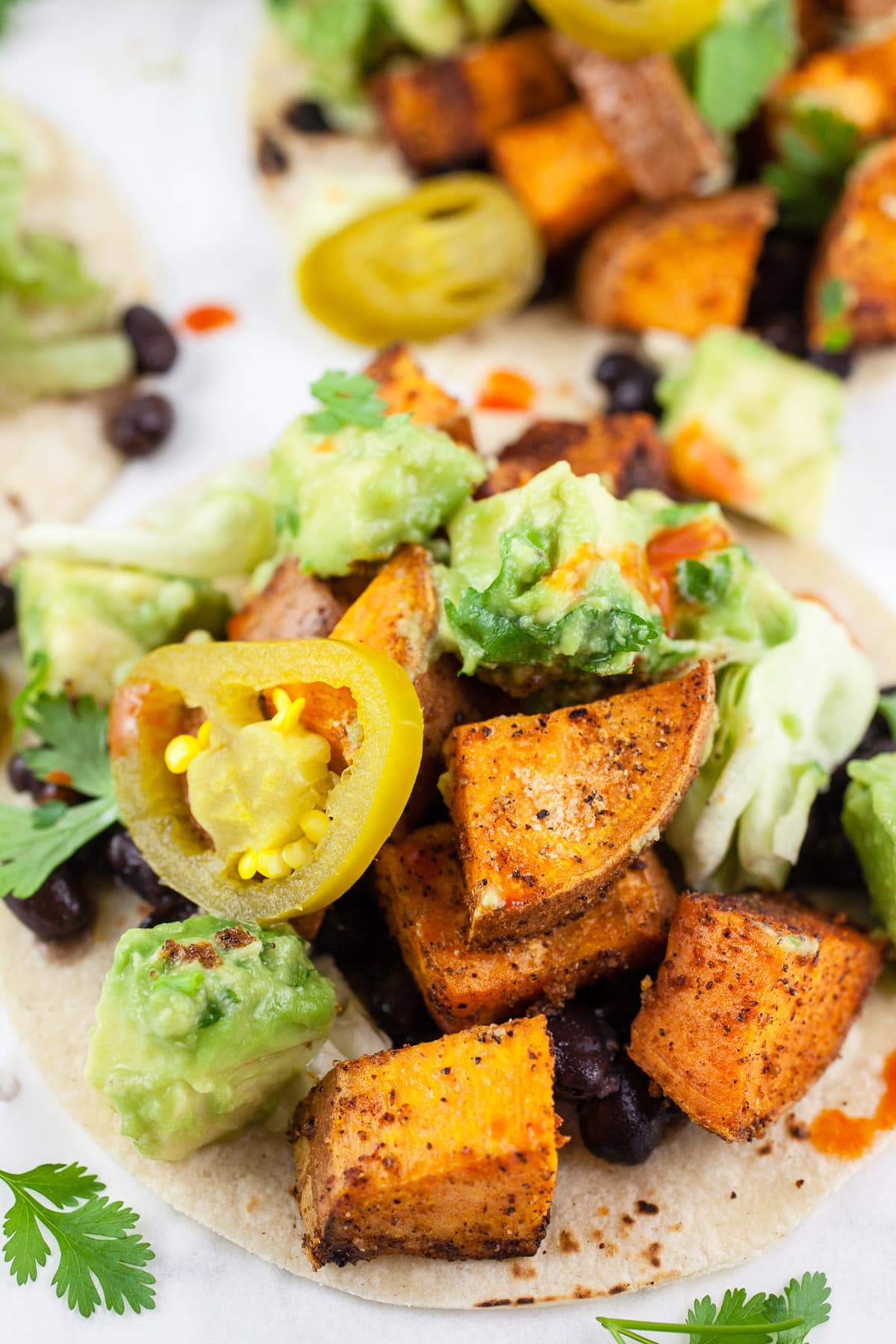 These Sweet Potato Tacos with Avocado Salsa make for a great weeknight dinner! This vegan sweet potato taco recipe is the perfect healthy clean eating dish. Sweet potatoes are topped with spices and then roasted until crispy in the oven. These vegetarian tacos are finished with black beans served with avocado salsa. Healthy eating doesn't get any easier than this! #sweetpotato #tacos #avocado #vegetarian #vegan Roasted sweet potato tacos with black beans and avocado salsa on corn tortillas.