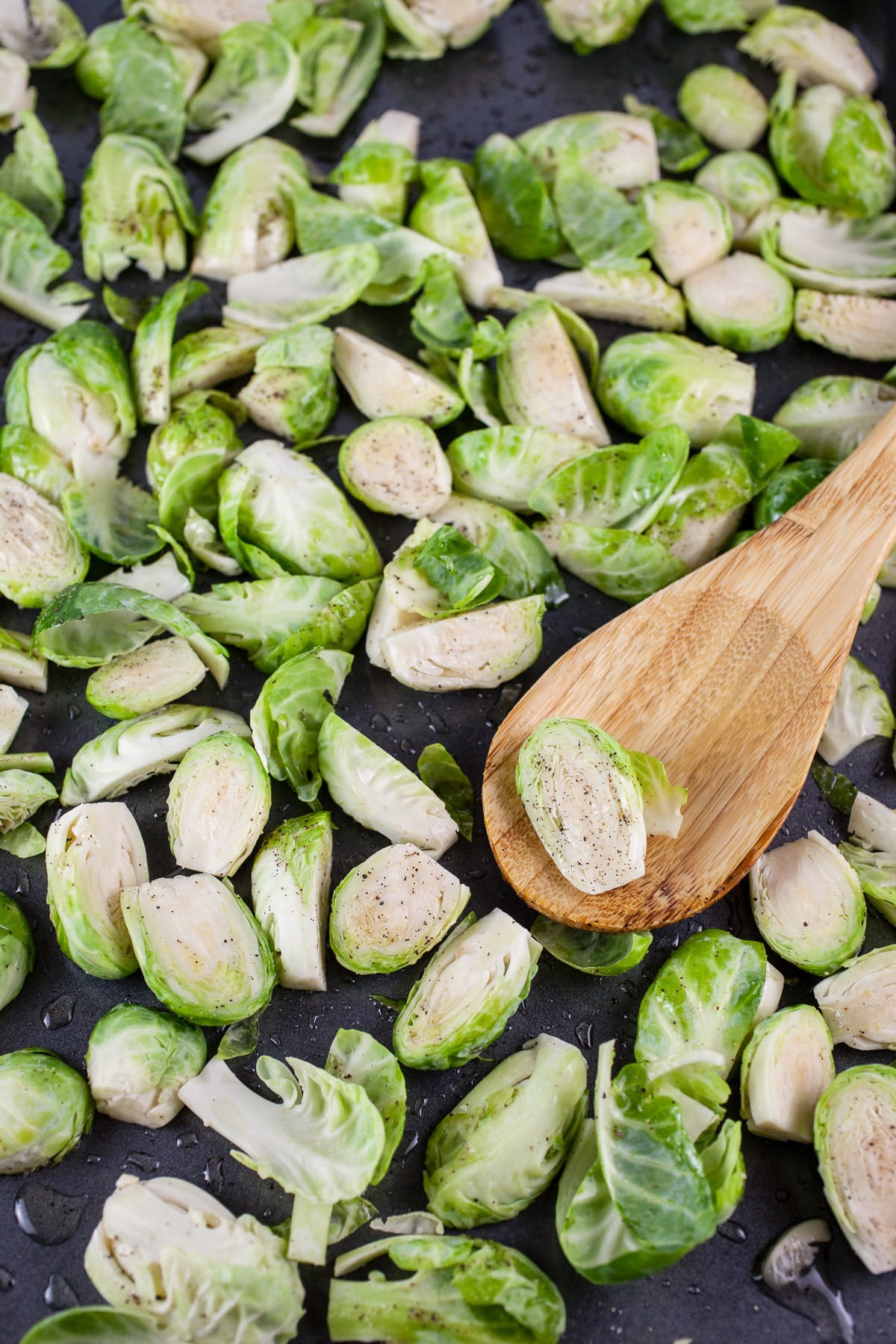 Uncooked chopped Brussels sprouts on baking sheet with wooden spoon.
