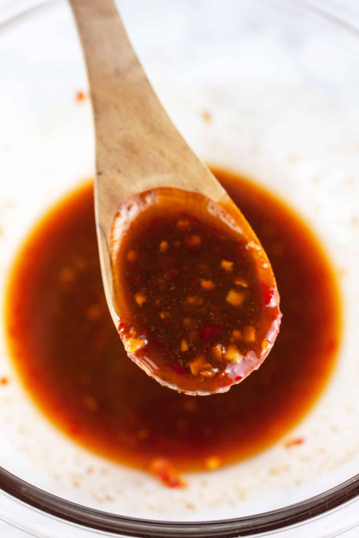 Sweet and spicy Asian sauce lifted from small glass bowl on wooden spoon.