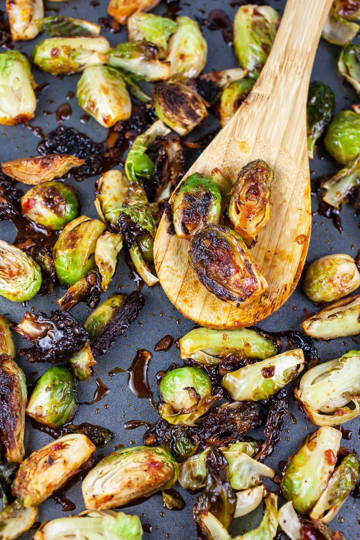 Cooked Asian glazed Brussels sprouts on baking sheet with wooden spoon.