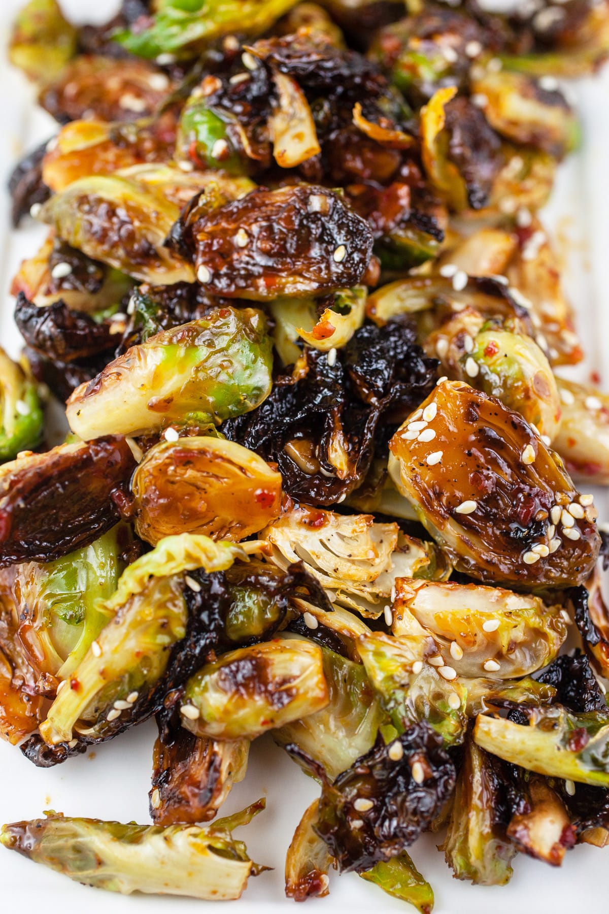 These Sweet and Spicy Roasted Brussels Sprouts are easy to make, healthy, and vegetarian. Learn how to cook brussels sprouts that are crispy and addictive! These simple brussels sprouts are roasted and baked in the oven and then finished with a sticky sweet honey and spicy garlic glaze. The Asian flavors in this side dish are the best! #brusselssprouts #recipes #vegetarian #easy #roasted #sidedish #spicy Asian roasted Brussels sprouts with sesame seeds on white platter.