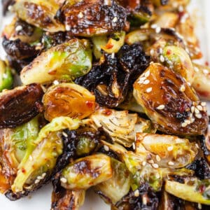 Sweet and spicy roasted Brussels sprouts with sesame seeds on white platter.