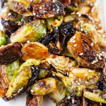 Sweet and spicy roasted Brussels sprouts with sesame seeds on white platter.