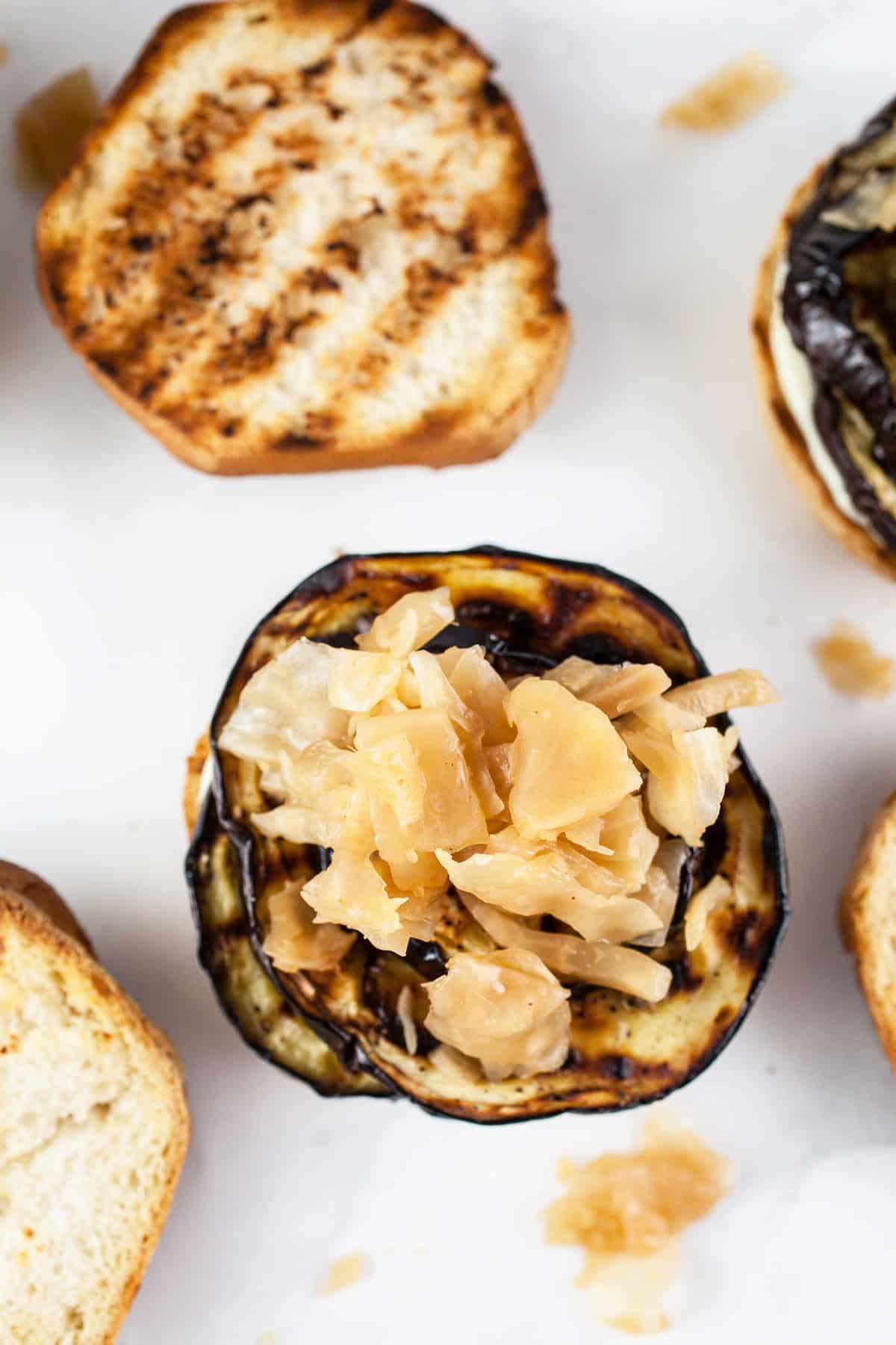 Toasted buns with grilled eggplant slices and kimchi on white surface.