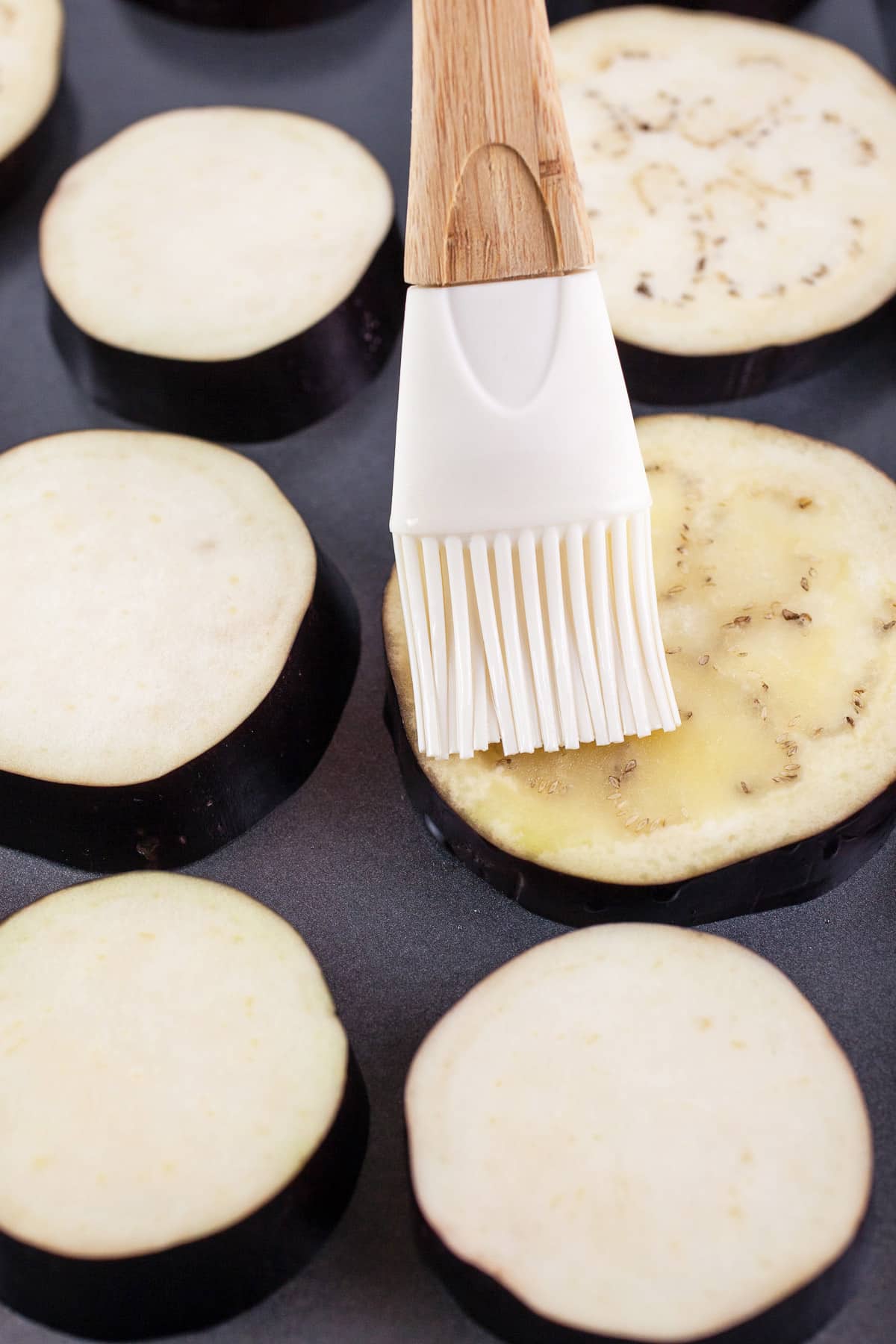 Olive oil brushed onto eggplant slices on baking sheet.