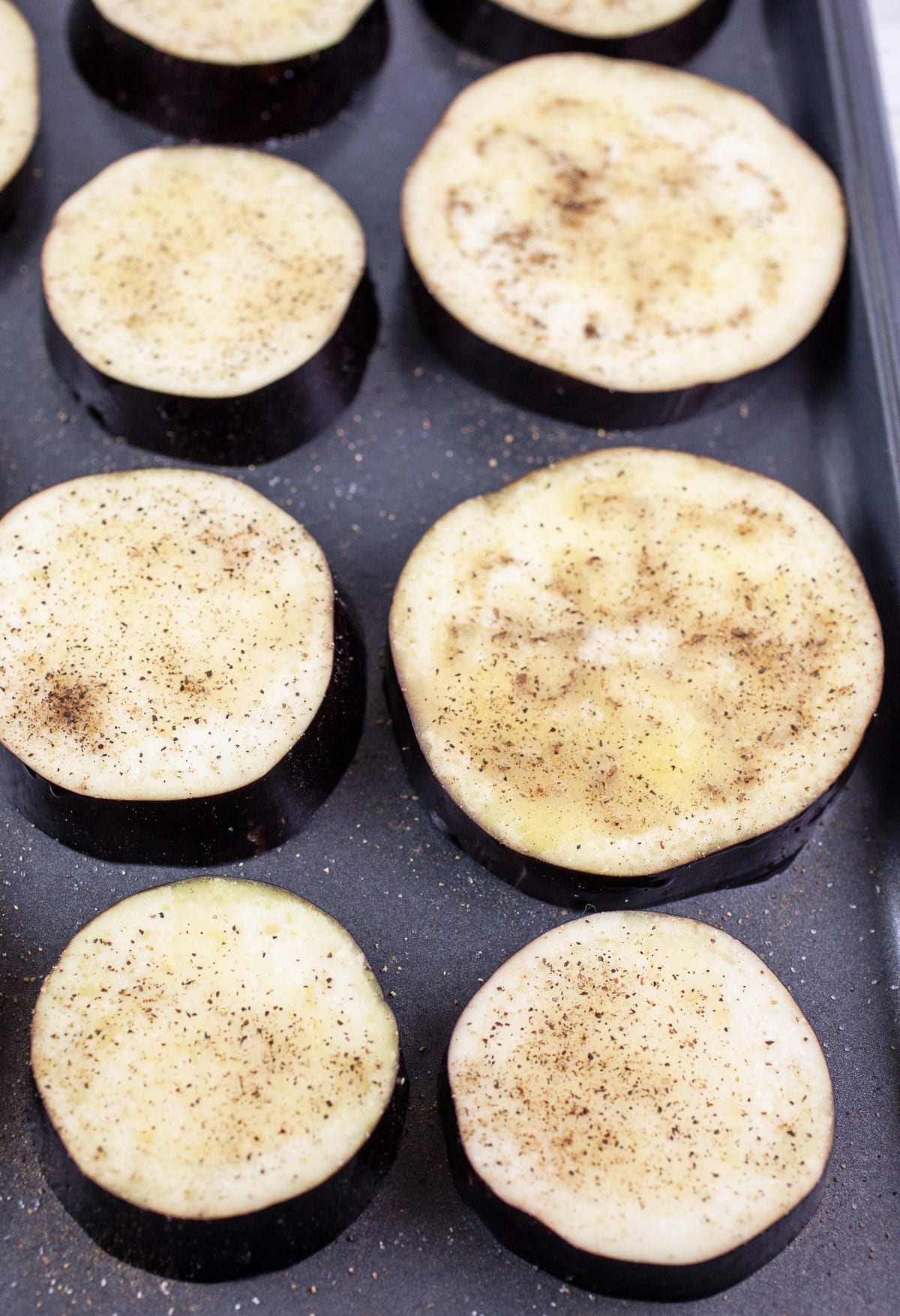 Eggplant slices with olive oil, salt and pepper on baking sheet.