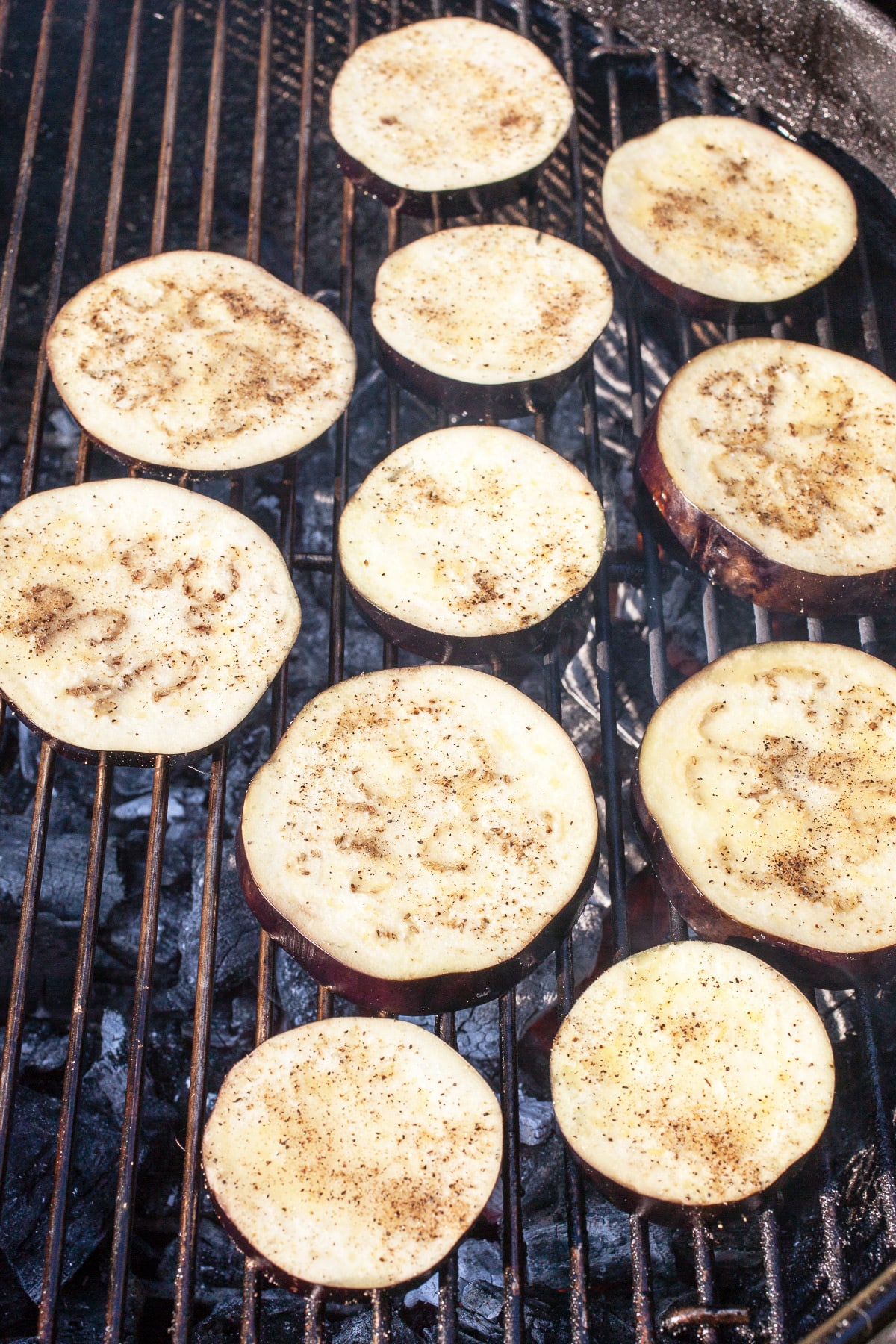 Uncooked eggplant slices on charcoal grill.