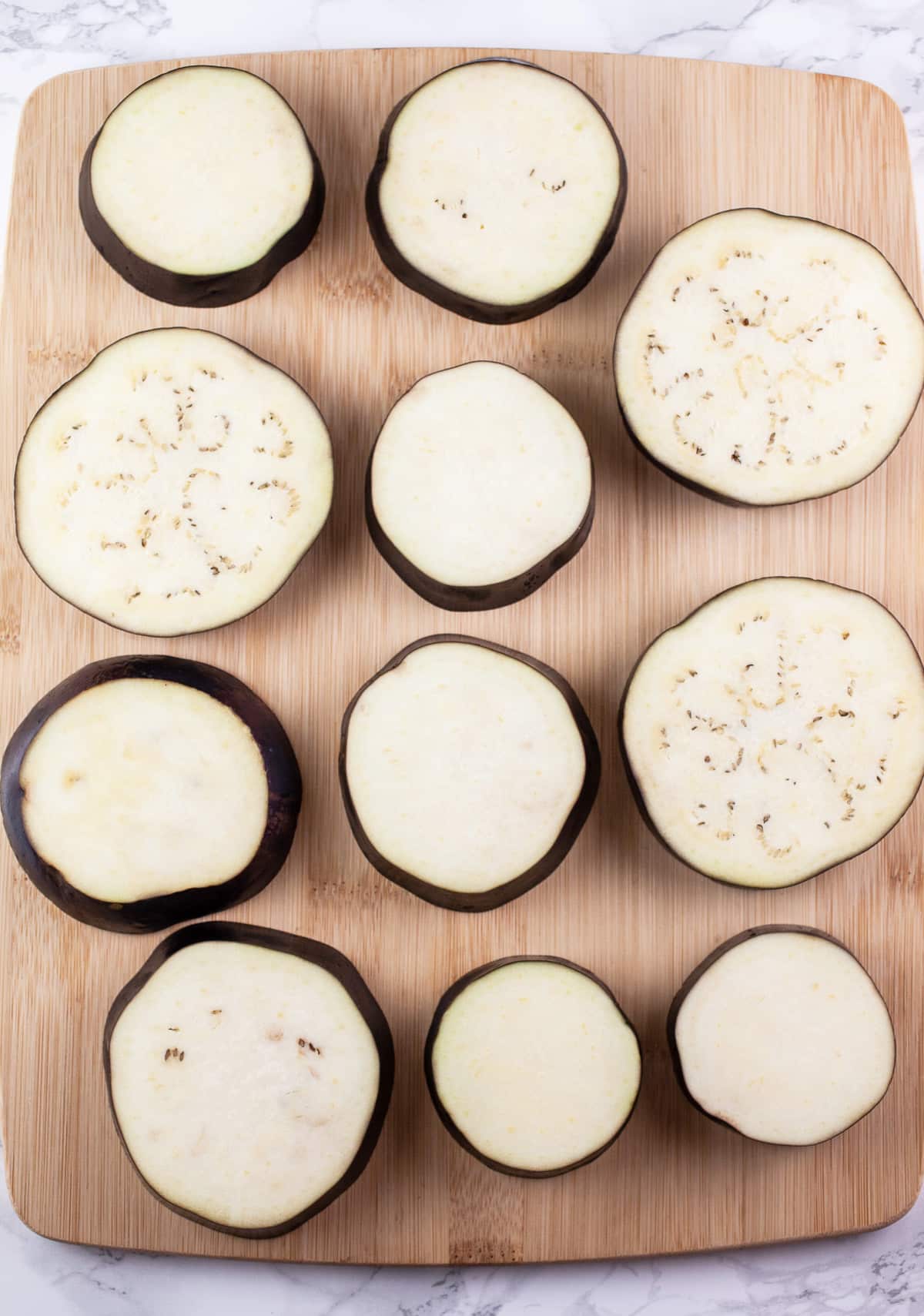 Eggplant slices on wooden cutting board.