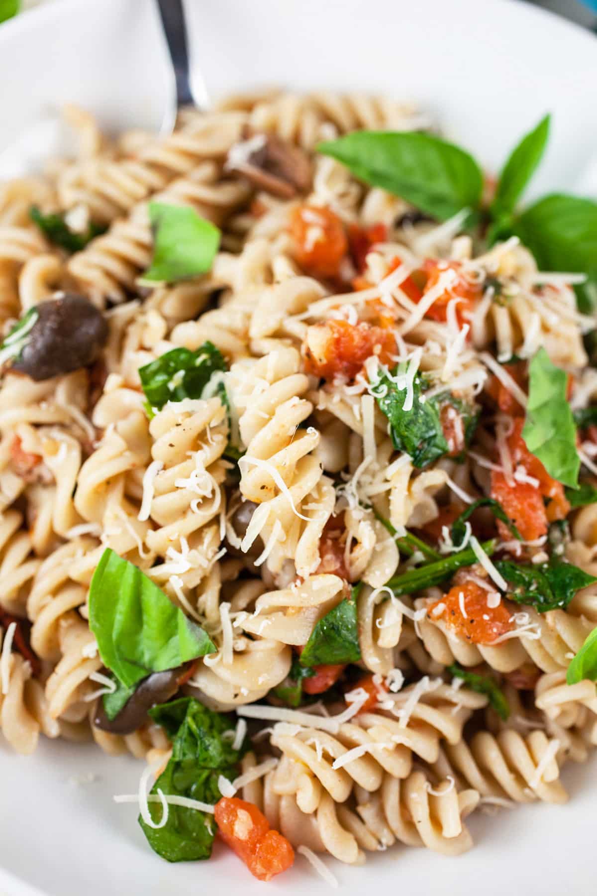 Vegetarian Mediterranean pasta with fresh basil and Parmesan cheese in white bowl with fork.