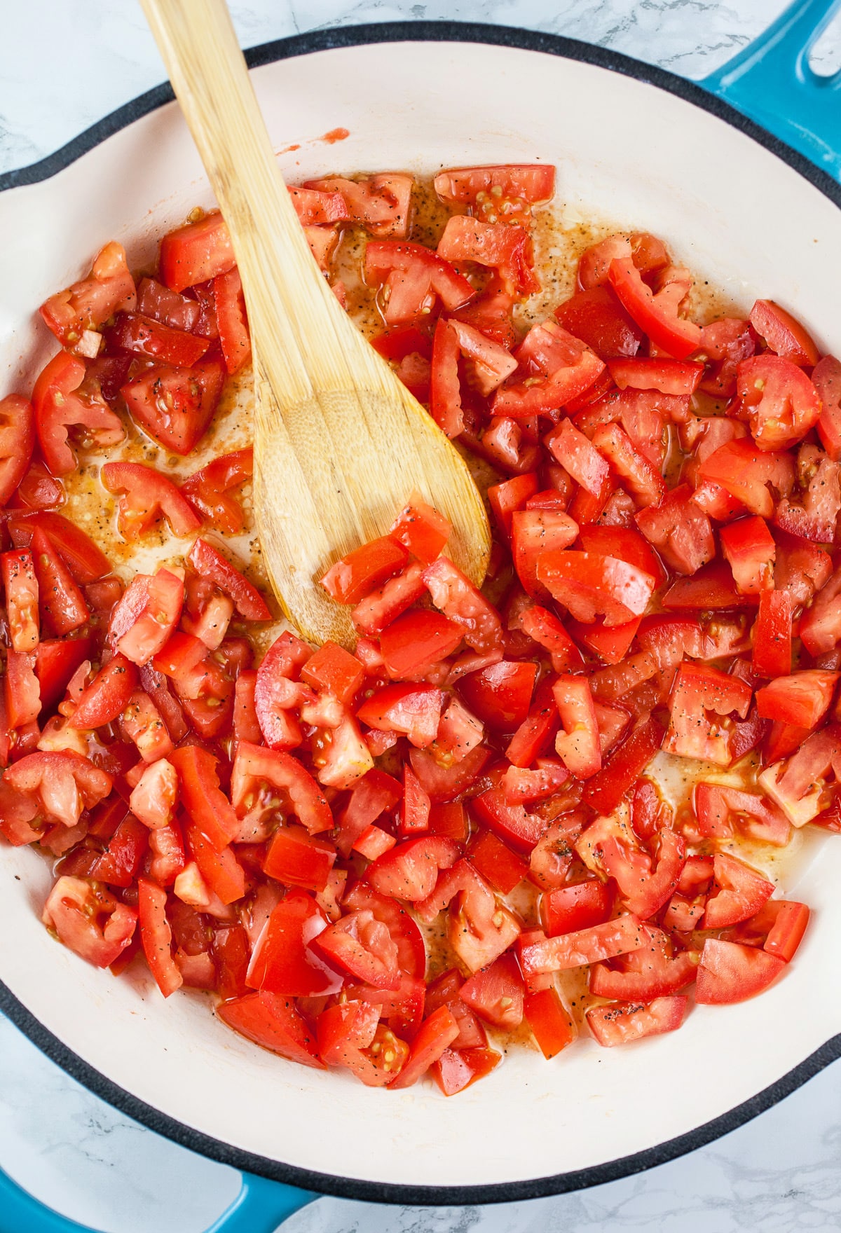 Diced tomatoes and garlic sautéed in skillet with wooden spoon. 