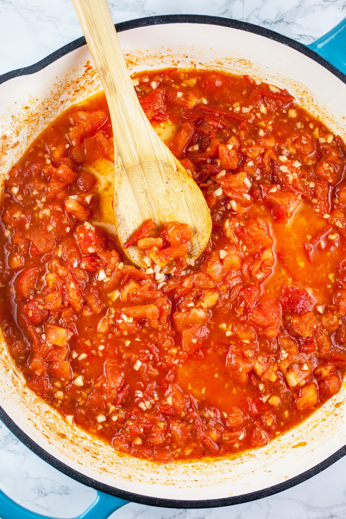 Diced tomatoes and garlic cooked down in skillet with wooden spoon.