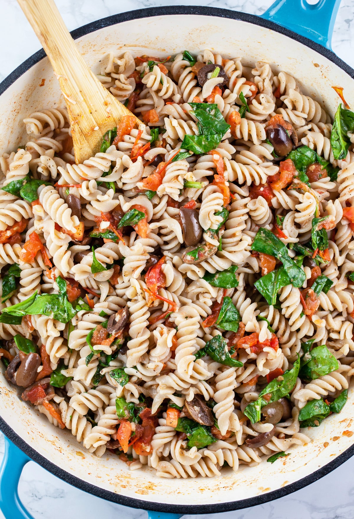 Vegetarian pasta combined in skillet with wooden spoon.