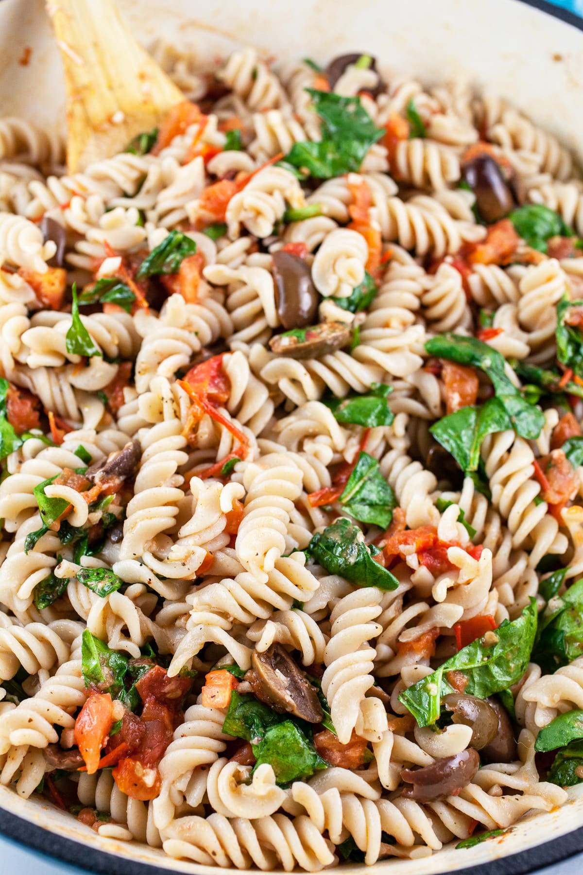 Mediterranean pasta combined in skillet with wooden spoon.