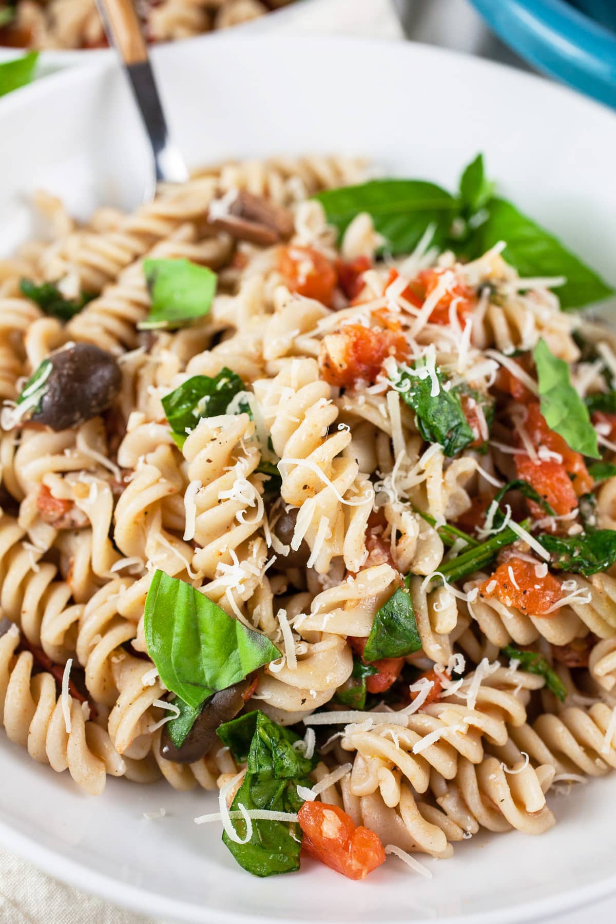 Vegetarian Mediterranean pasta with fresh basil and Parmesan cheese in white bowl with fork.