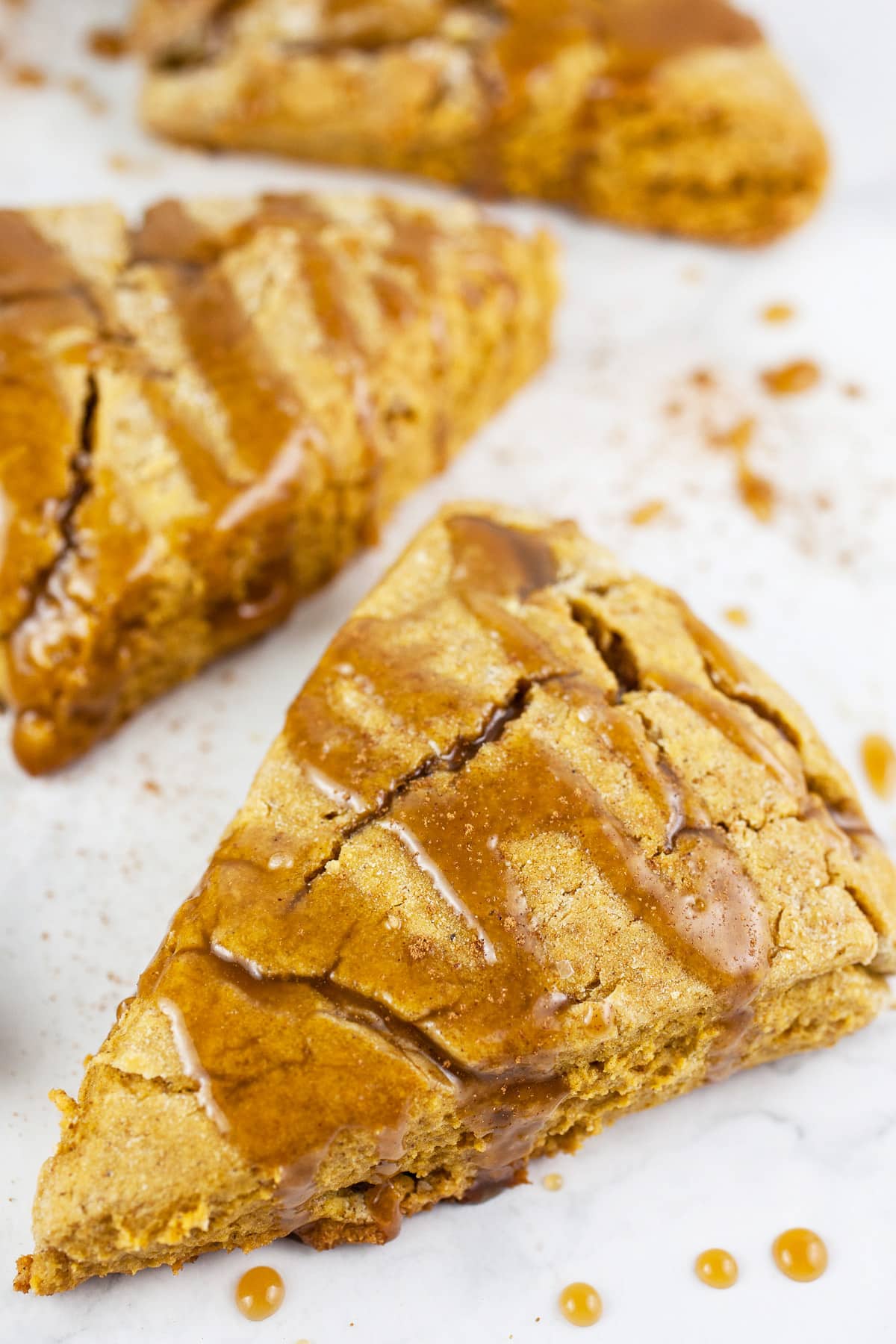 Pumpkin scones with maple glaze on white surface.