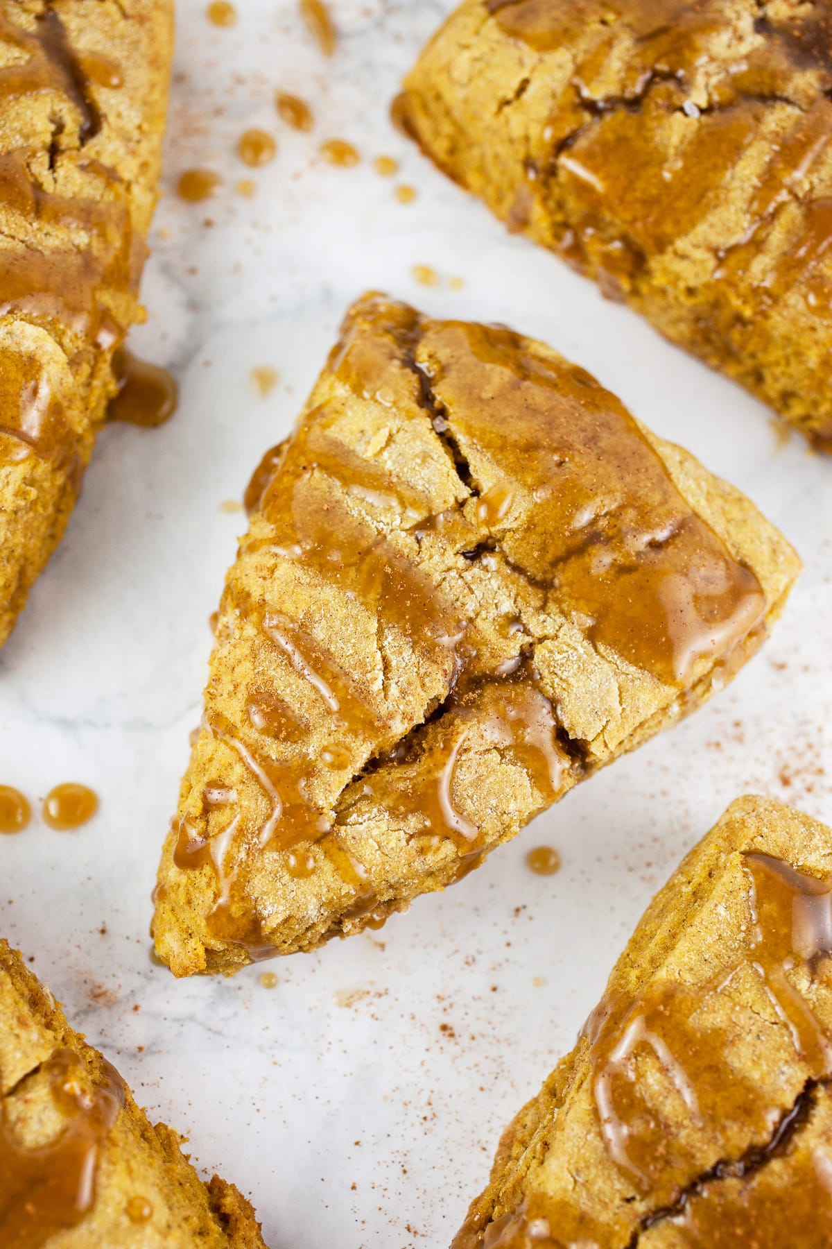 Gluten free pumpkin scones with maple caramel glaze on white surface.