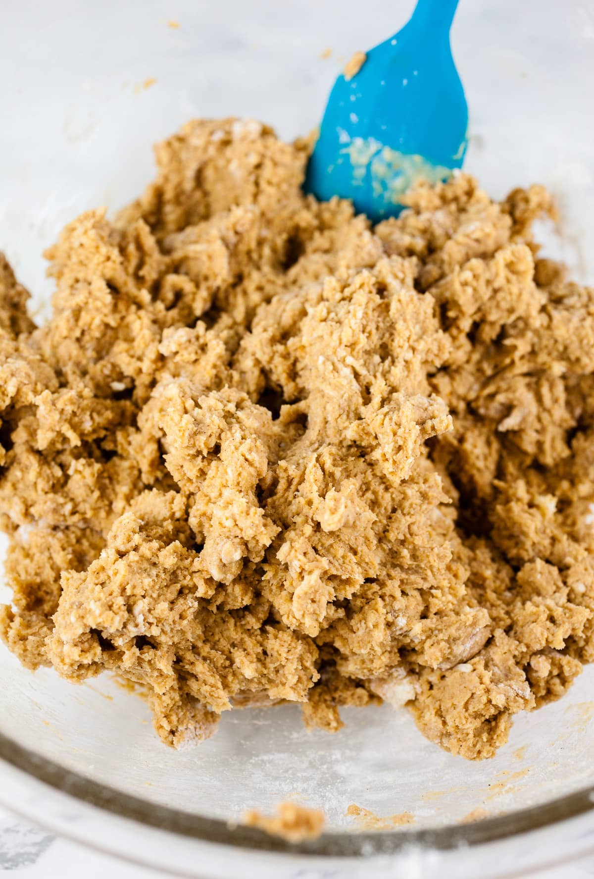 Pumpkin scone batter in large glass bowl with blue spatula.