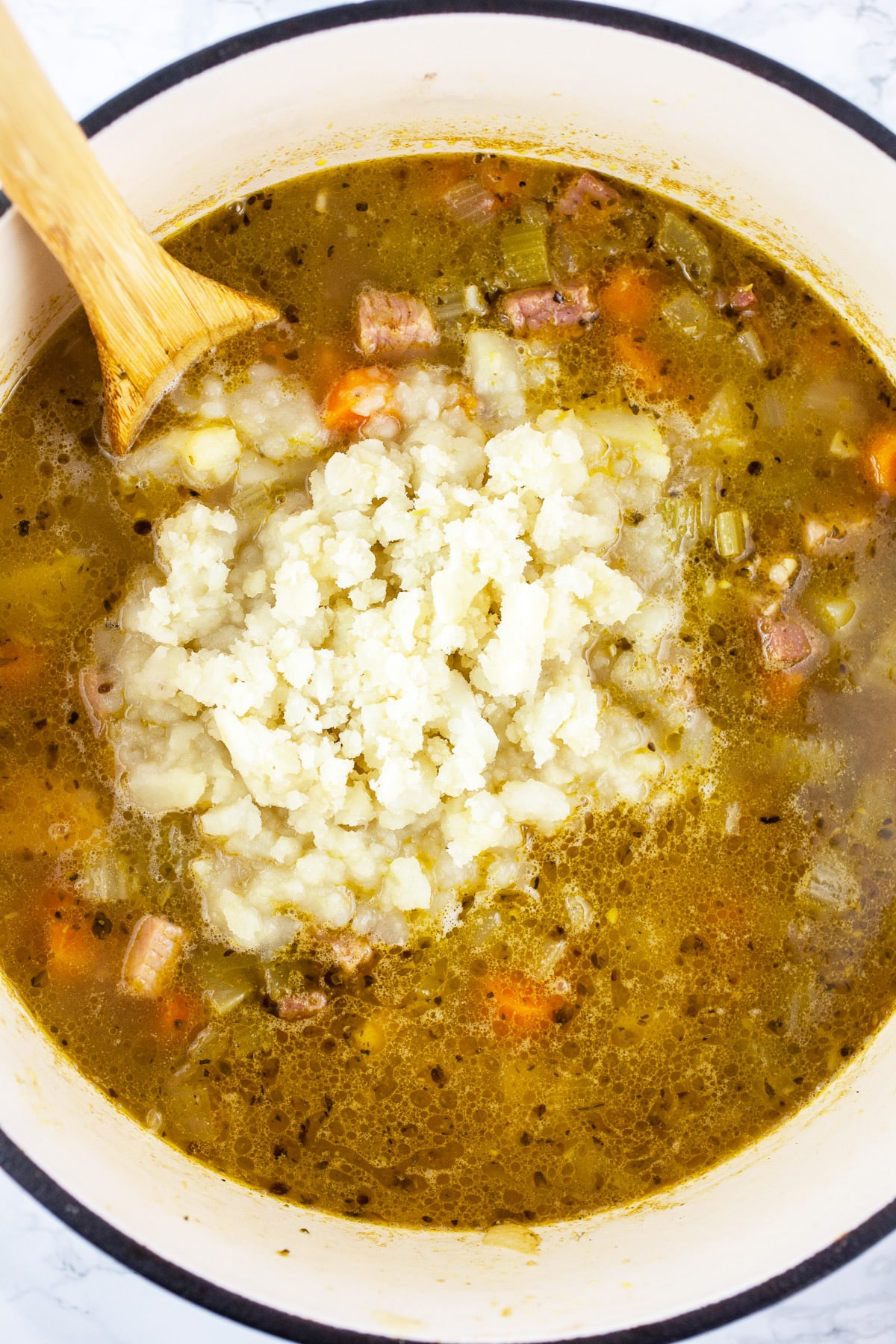 Mashed potatoes added to soup in Dutch oven.