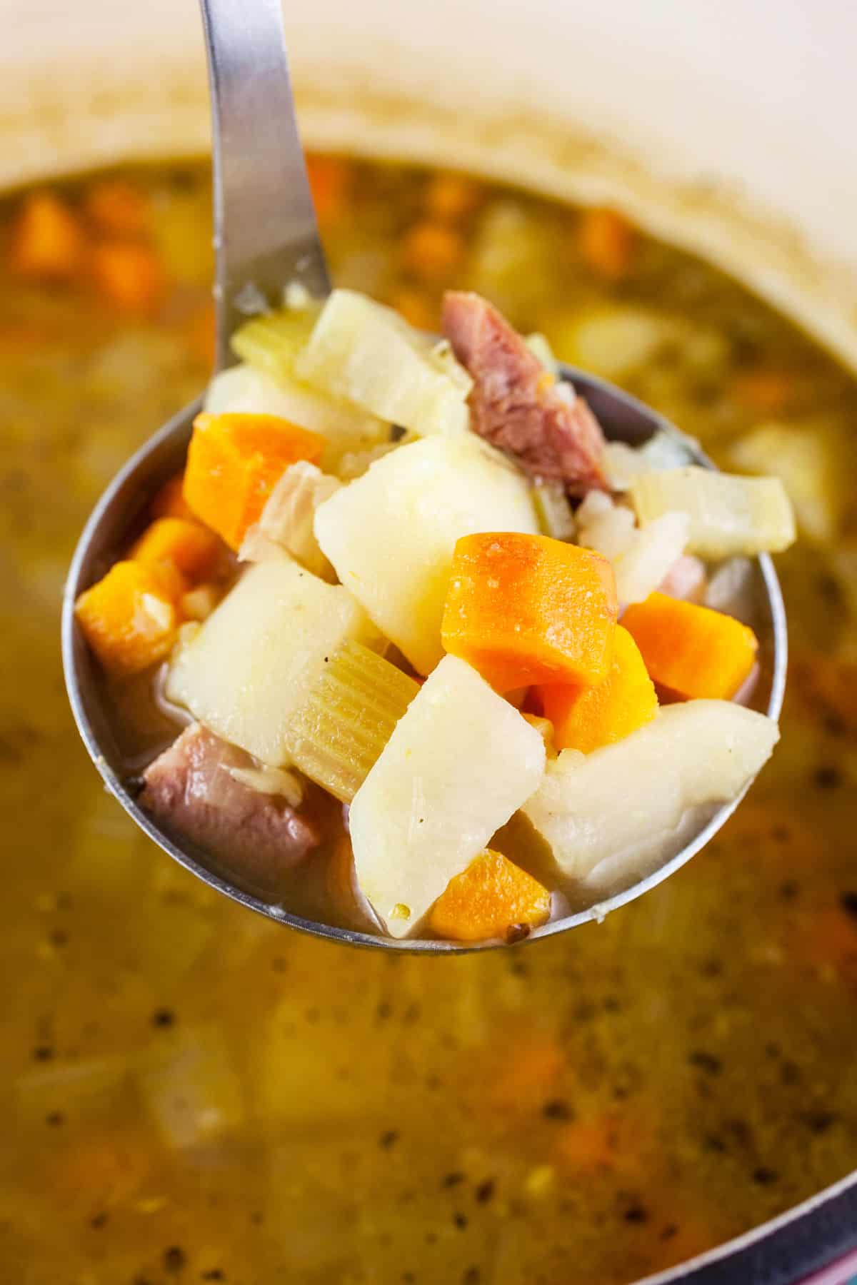 Scoop of ham potato soup lifted from Dutch oven on metal ladle.