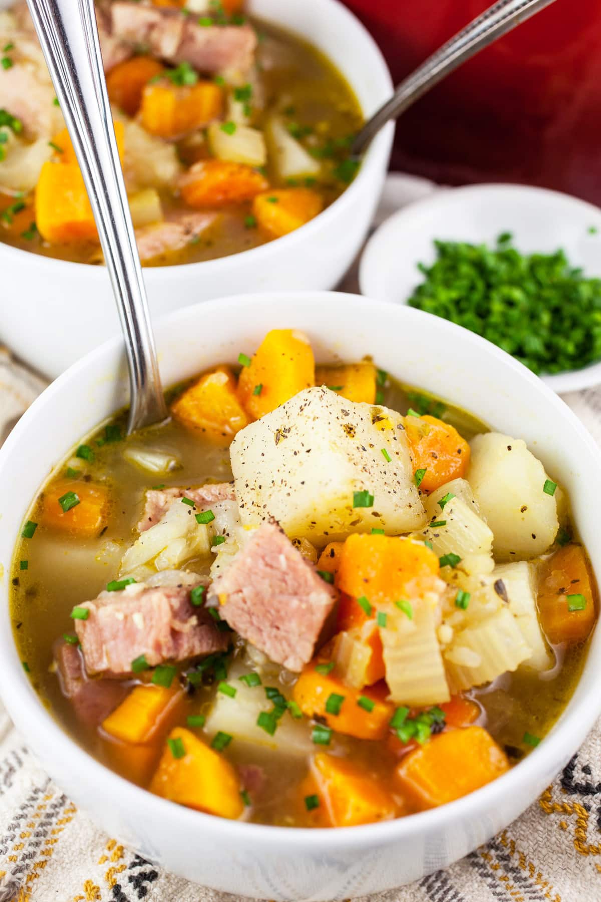 Ham and potato soup with minced chives in white bowls with spoons.