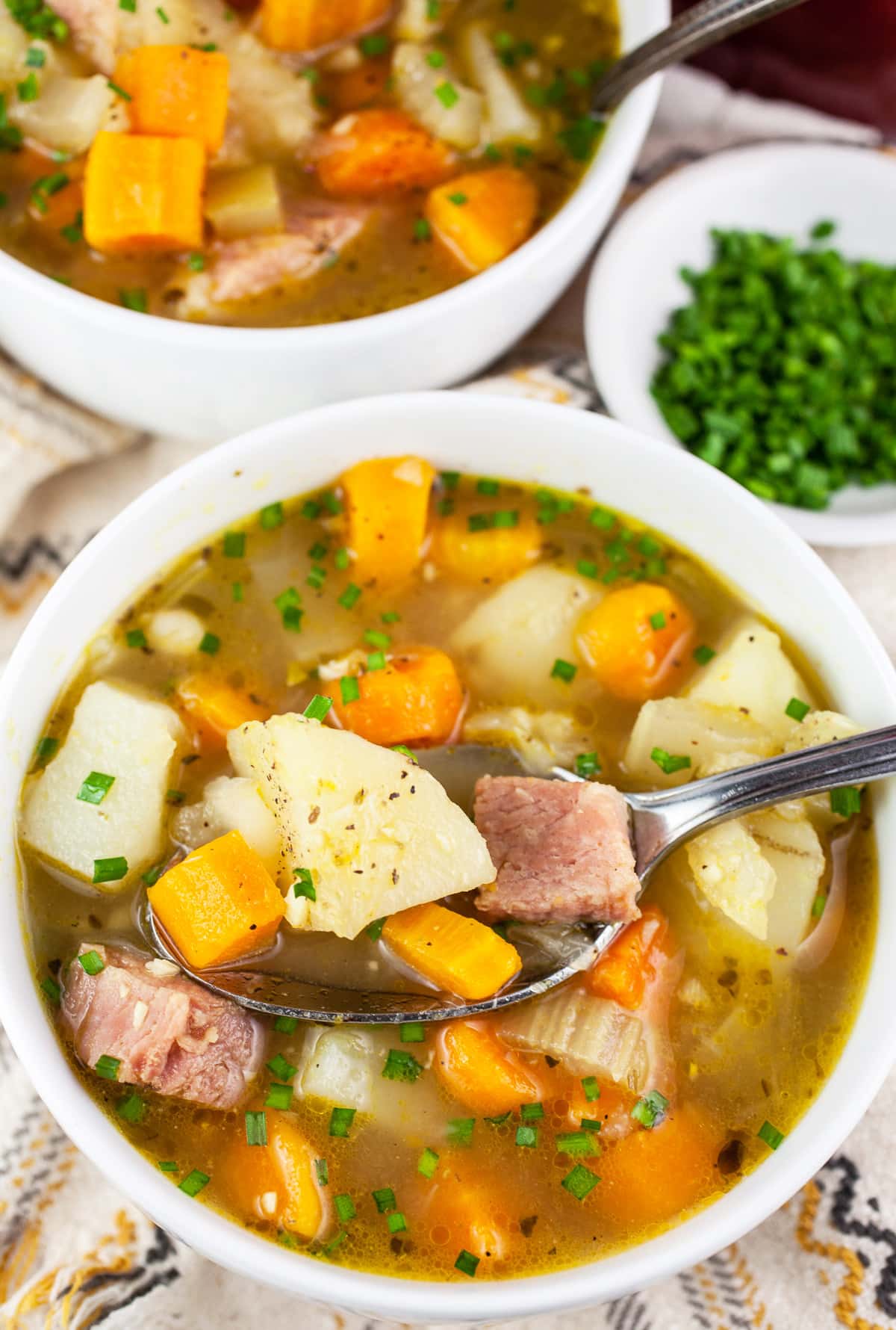 Ham and potato soup in white bowls with minced chives.