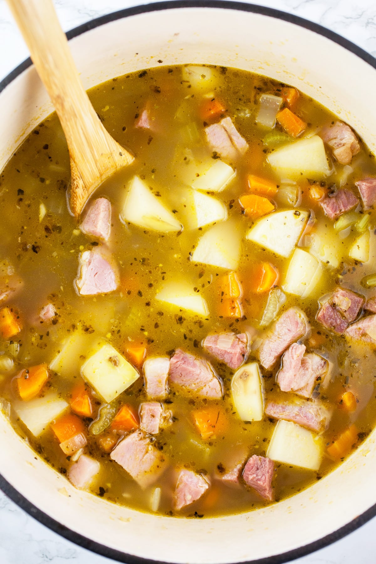 Potato ham soup in Dutch oven with wooden spoon.