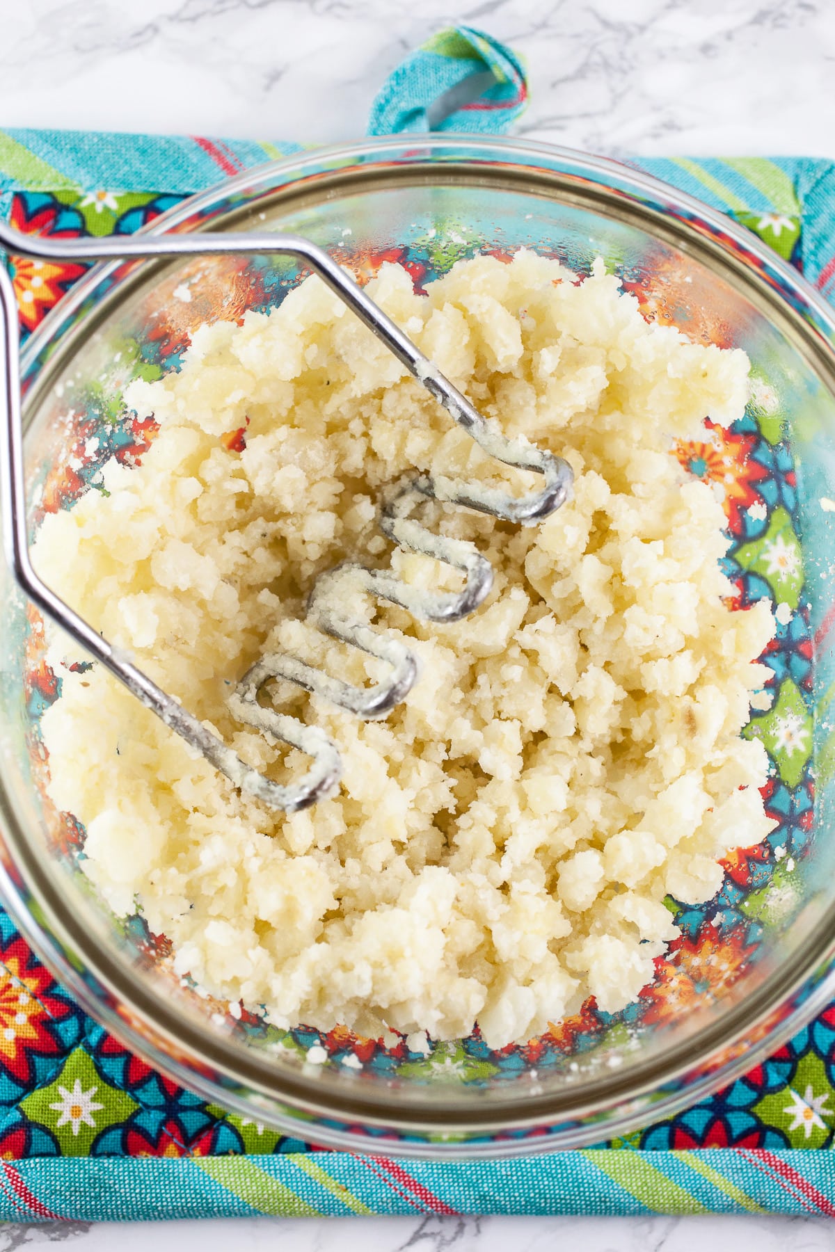 Mashed potatoes in small glass bowl on colorful potholder.