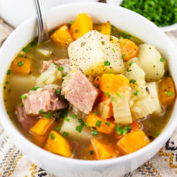 Ham and potato soup in white bowl with spoon.