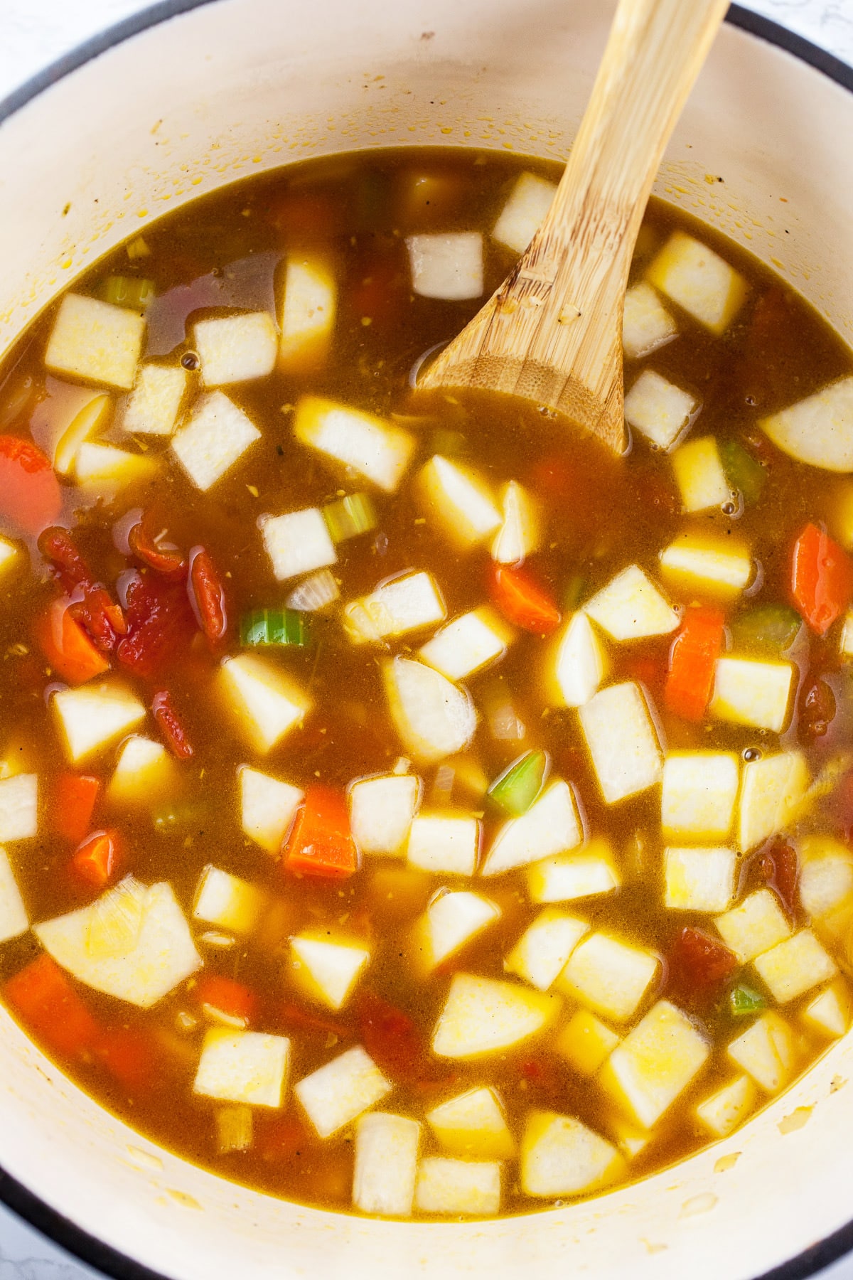 Uncooked vegetable soup in Dutch oven with wooden spoon.