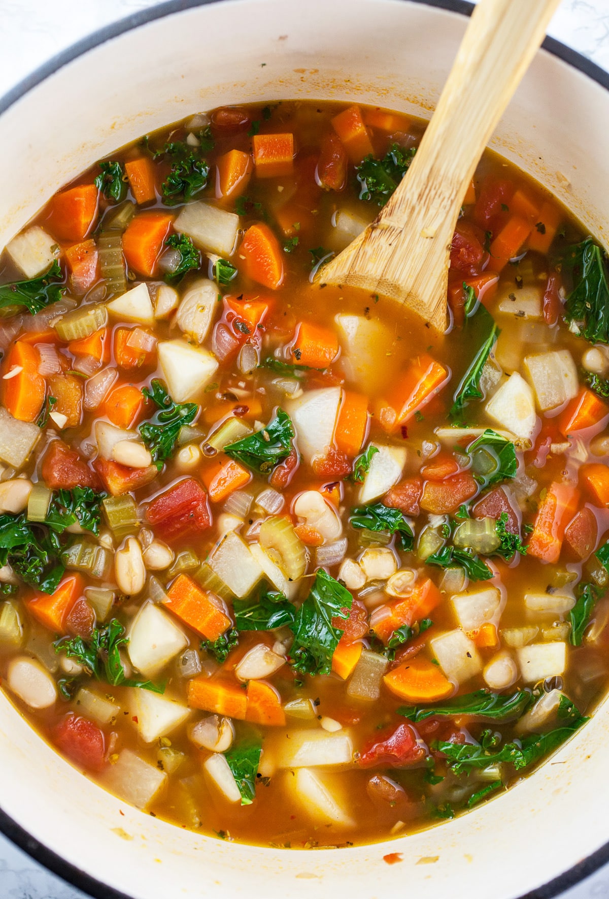 Cooked vegetable soup in Dutch oven with wooden spoon.