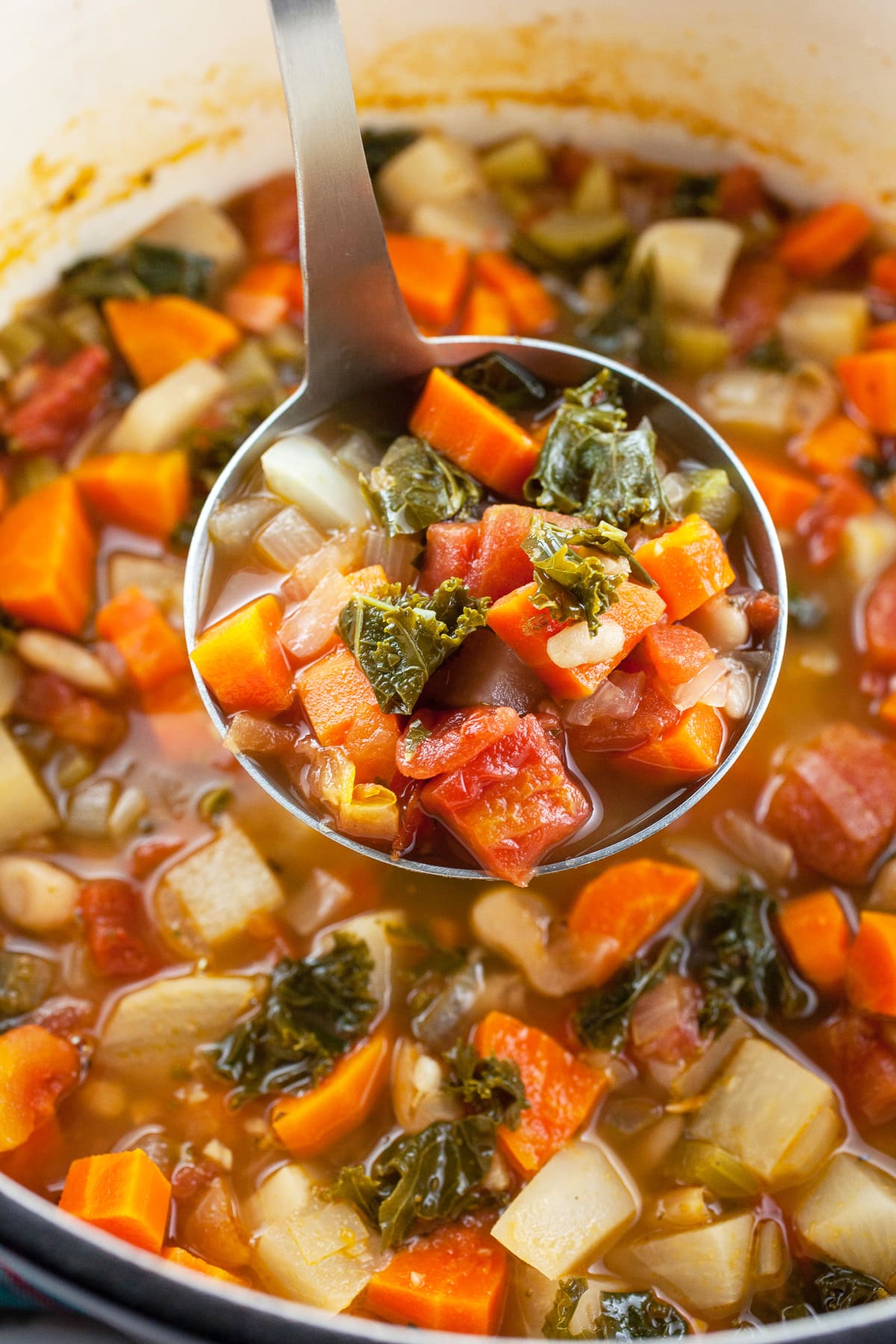 Scoop of vegetable soup lifted from Dutch oven with metal ladle.