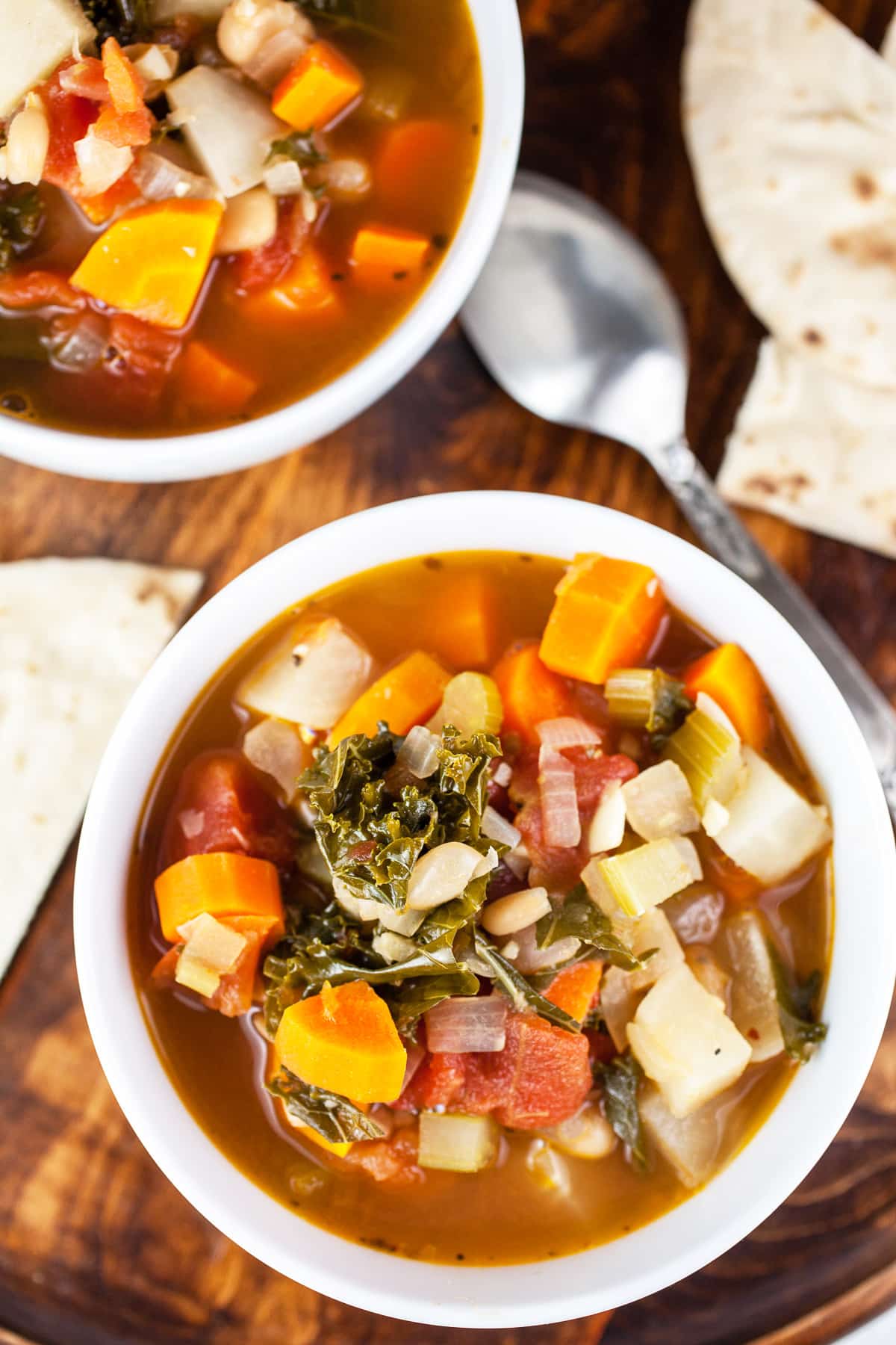 Healthy vegetable soup in white bowls with sliced pita bread on wooden tray.