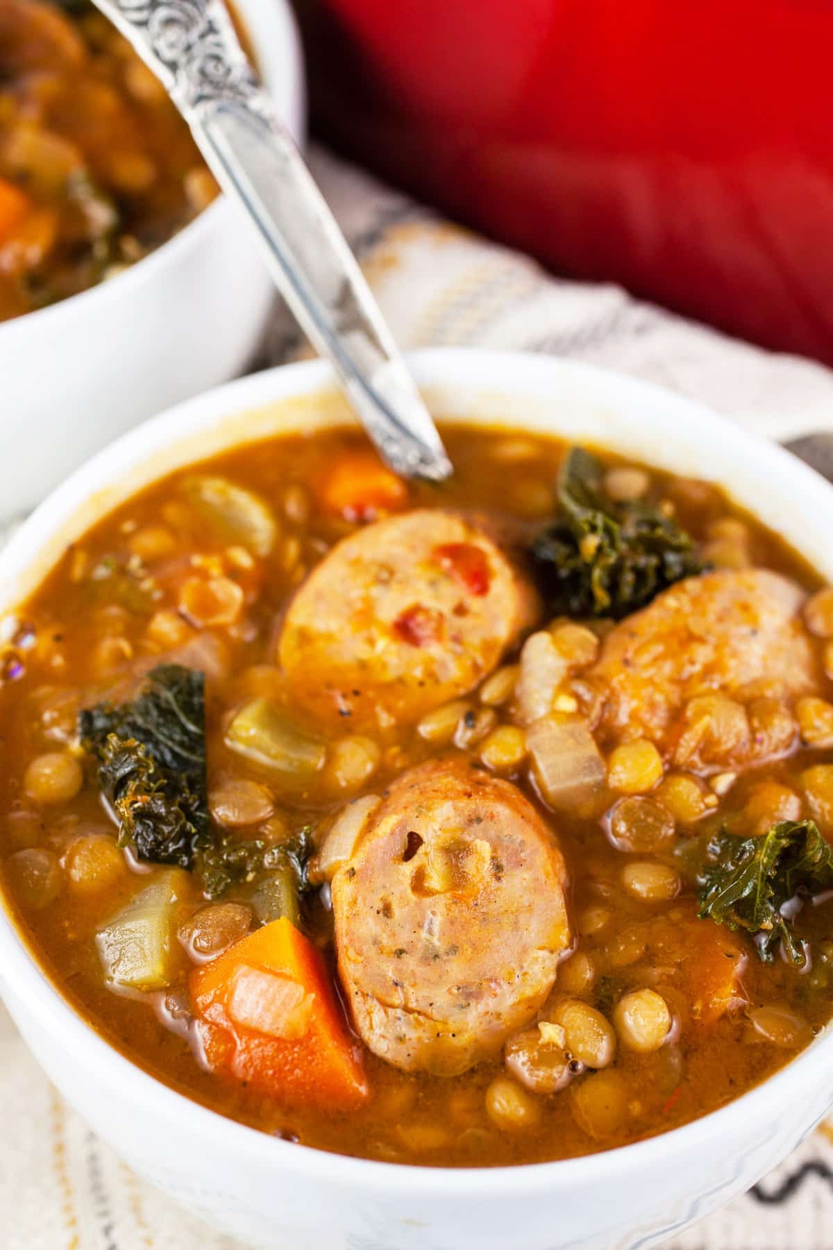 Sausage lentil kale soup in white bowl with spoon.