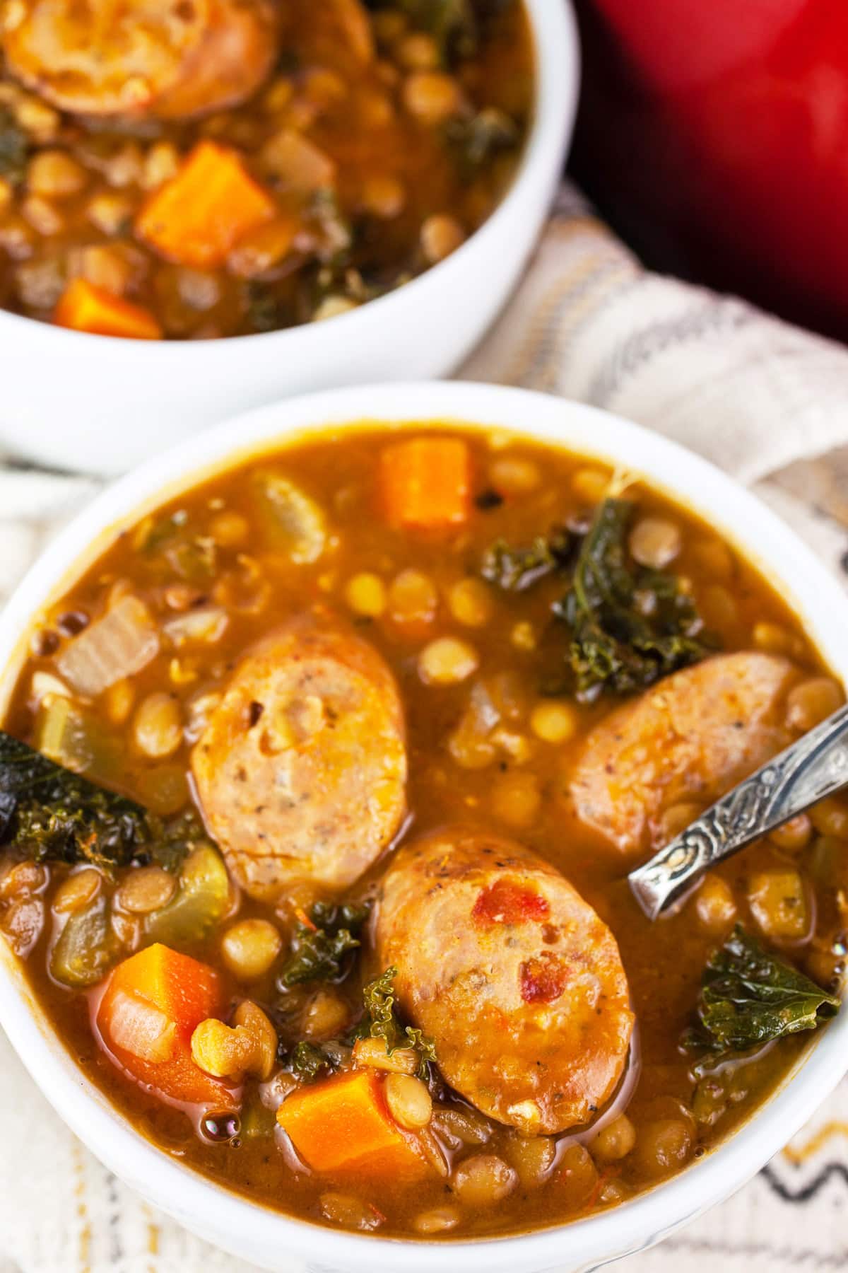 Sausage lentil kale soup in white bowls with spoon.