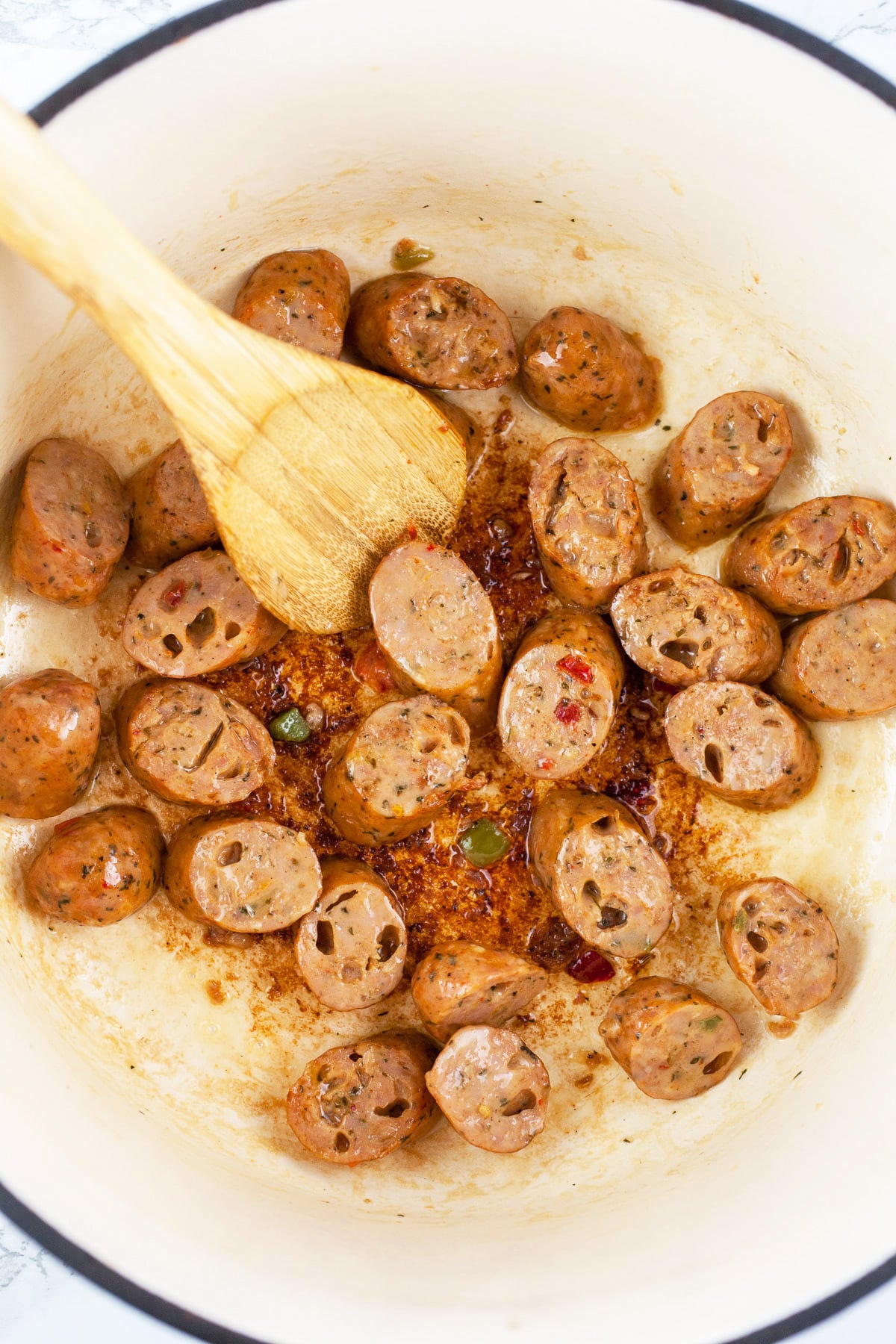 Sliced chicken sausages sautéed in Dutch oven with wooden spoon.