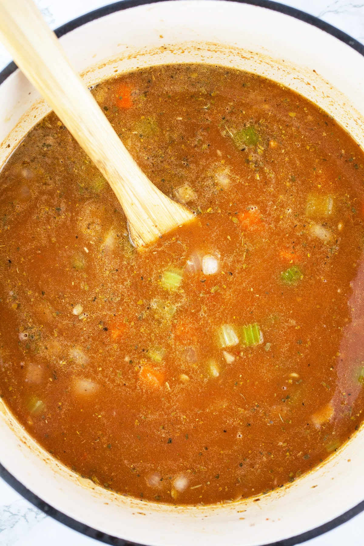 Uncooked lentil soup in Dutch oven with wooden spoon.