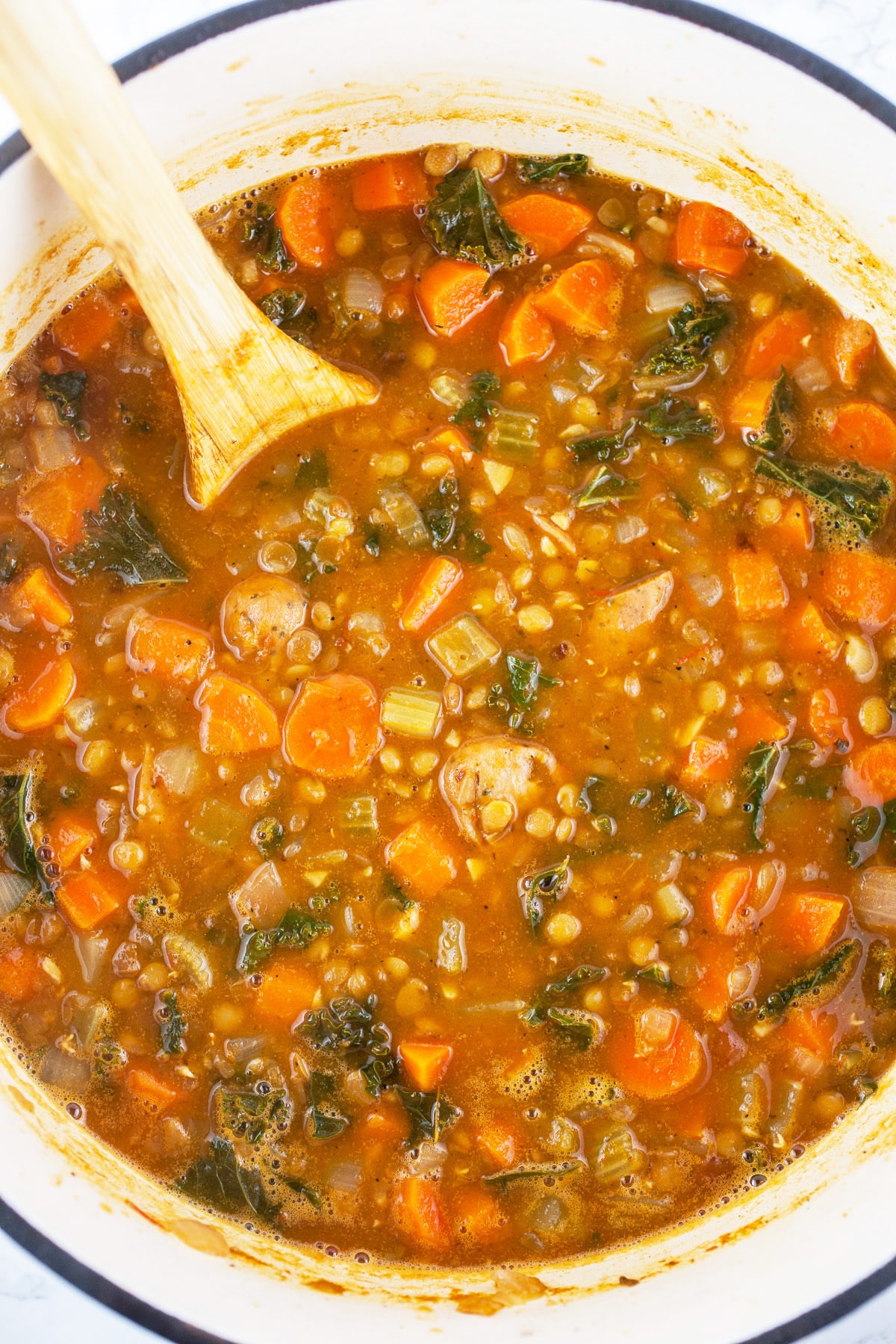 Cooked lentil sausage soup in Dutch oven with wooden spoon.