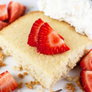 Slice of Scandinavian almond cake with whipped cream and strawberries on white plate.