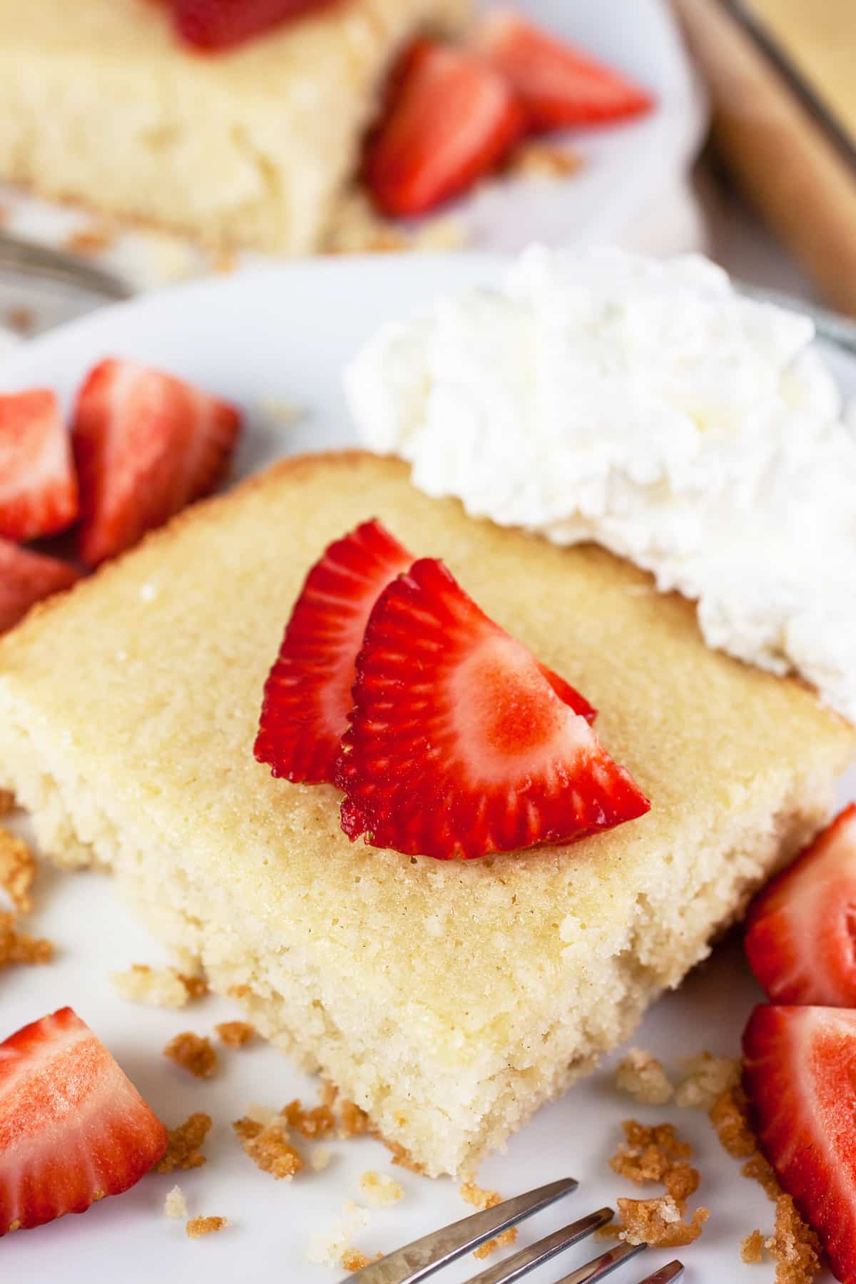 This Scandinavian Almond Cake with Coconut Whipped Cream is my go-to cake recipe! It's easy to make, moist, and topped with the best homemade coconut whipped cream. This cake is made from scratch and comes from an old church cookbook. Finish it of with fresh strawberries and you've got the perfect summer dessert! #cake #Scandinavian #almond #coconut #whipped cream #homemade #easy Scandinavian almond cake with whipped cream and strawberries on white plates.